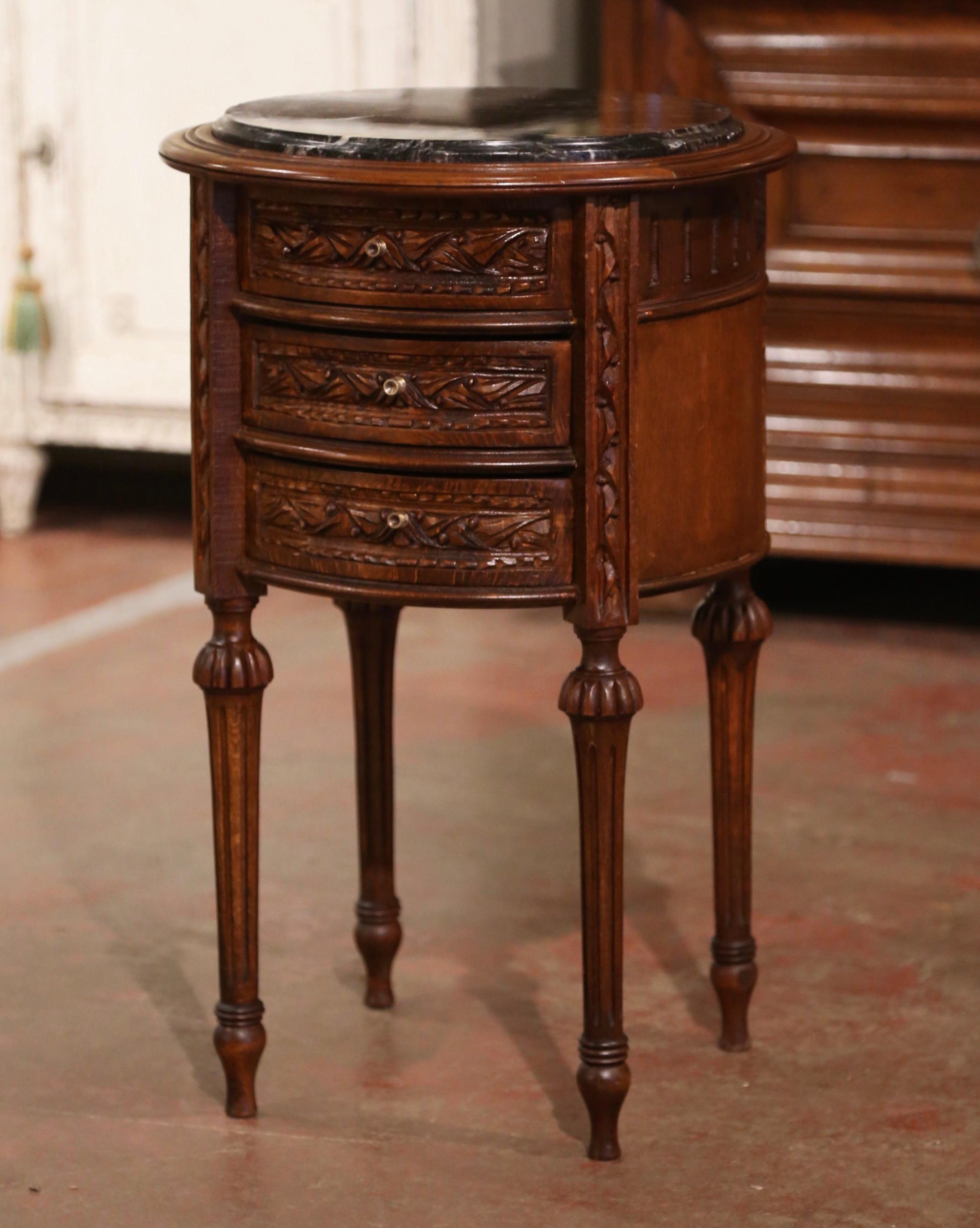 This elegant antique side table was created in France circa 1960. Built of walnut and round in shape, the table stands on tapered fluted legs ending with turned feet. The petite table features three carved drawers decorated with brass knobs. The