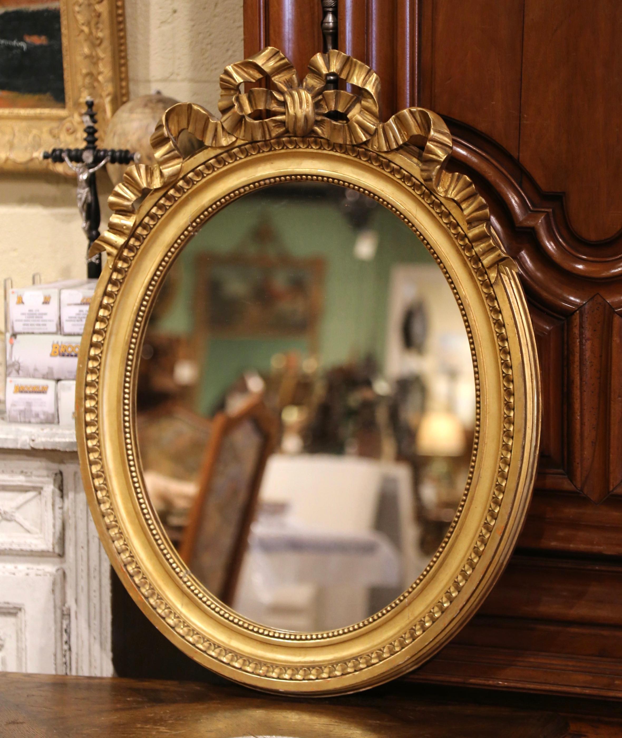 Decorate a powder room or entryway with this elegant antique wall mirror. Crafted in France, circa 1950, the oval frame is decorated with the traditional Louis XVI ribbon bow at the pediment, and embellished with geometric motifs around the frame