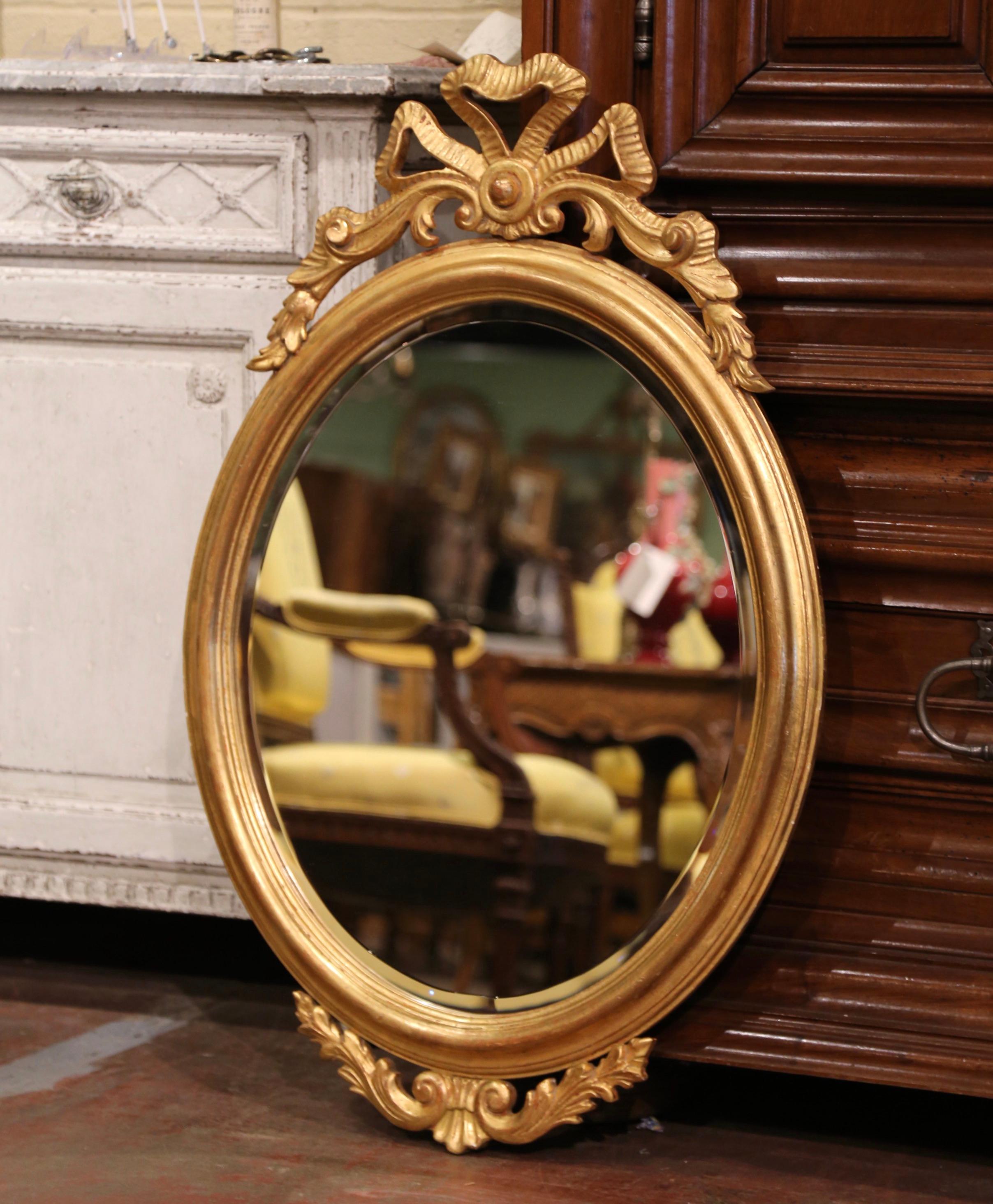 Decorate a powder room or entryway with this elegant antique wall mirror. Crafted in France, circa 1960, the oval frame is decorated with the traditional Louis XVI ribbon bow at the pediment, and embellished with leaf motifs at the bottom. The large
