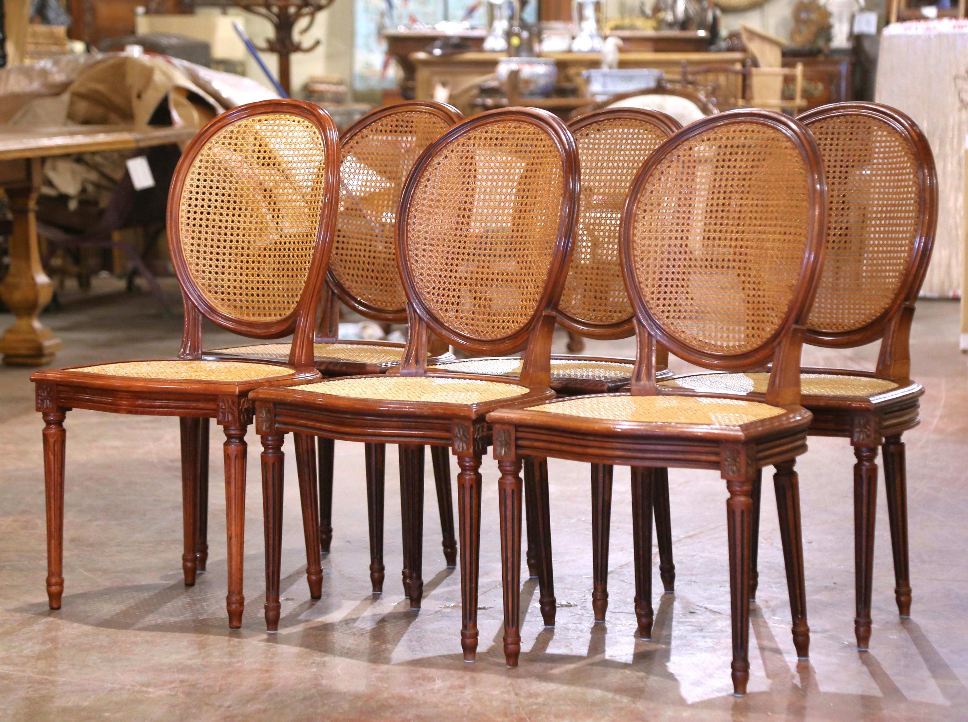 Decorate a dining table with this elegant suite of six antique side chairs. Crafted in France circa 1960 and built from solid walnut, each chair stands on fluted and tapered legs accented with carved floral rosette medallions at the shoulders. The