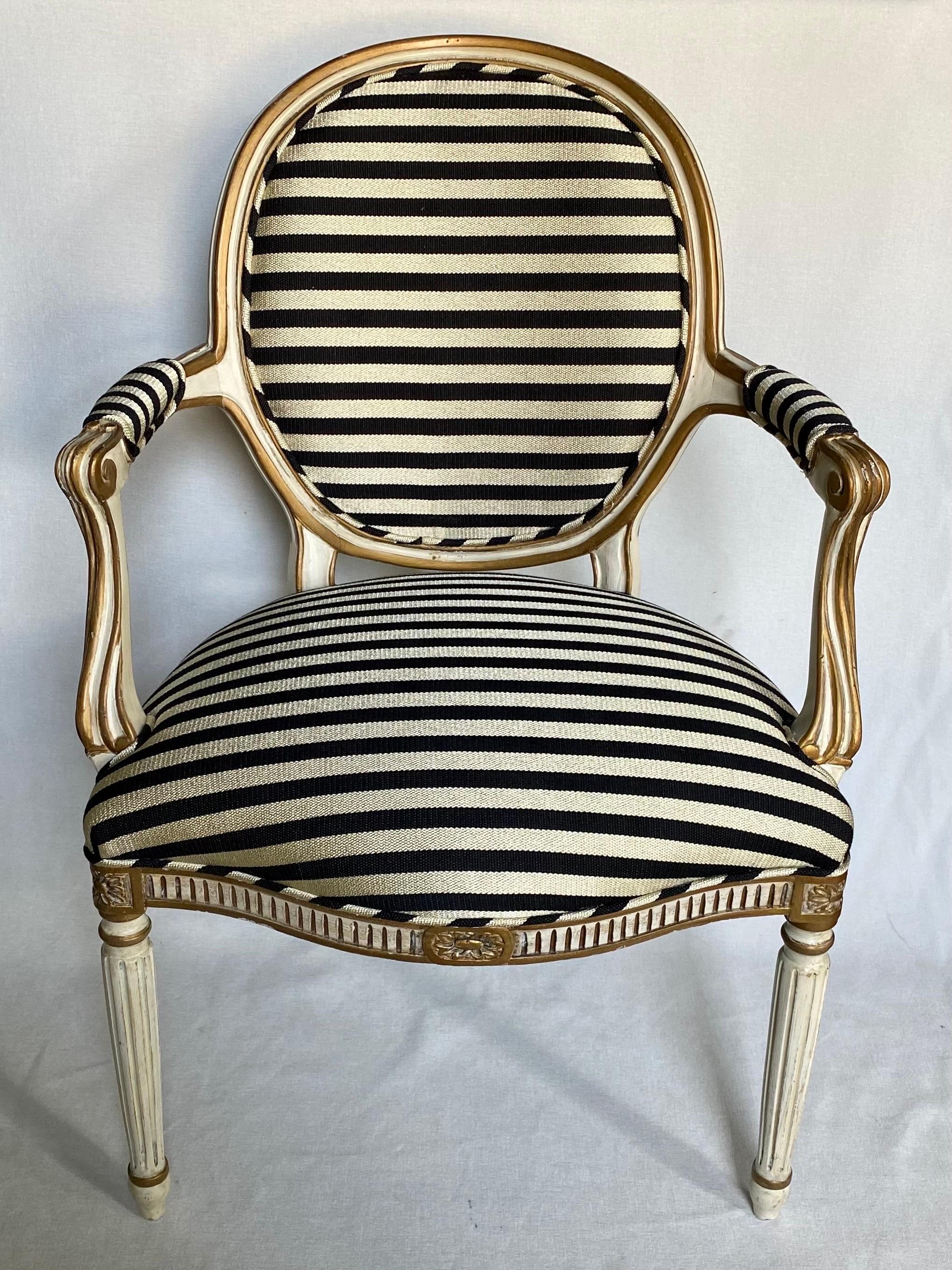 French Louis XVI style cream and gilt painted wood armchair custom upholstered in a fabulous Geoffrey Beene inspired striped fabric by Schumacher. This round back chair features beautifully carved and fluted details with a generous sized seat. The
