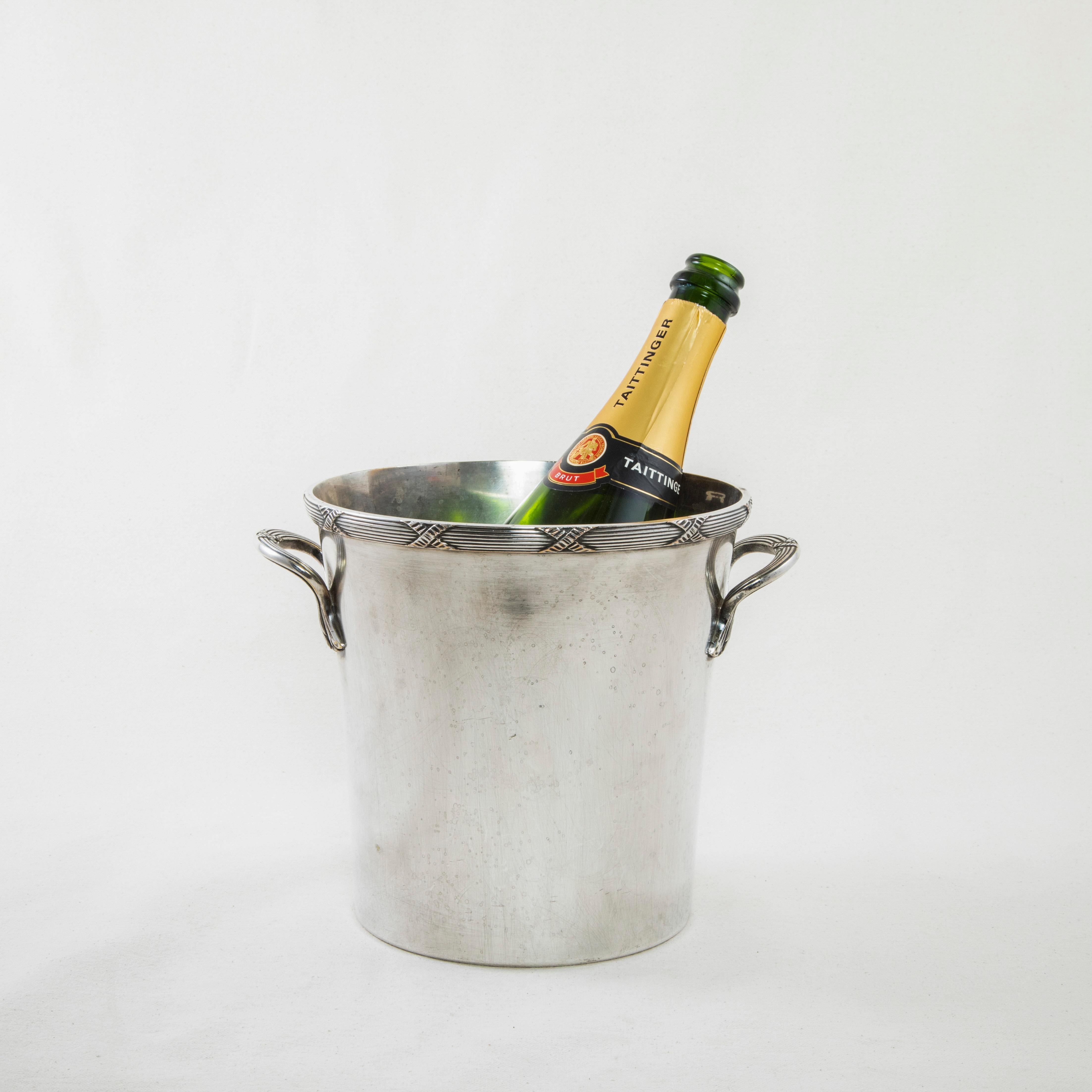 This French silver plate champagne bucket or wine chiller features a fluted upper rim detailed with Louis XVI crossed ribbons. Two handles with stylized leaves are further detailed with the Louis XVI motif. It is stamped on the bottom with the