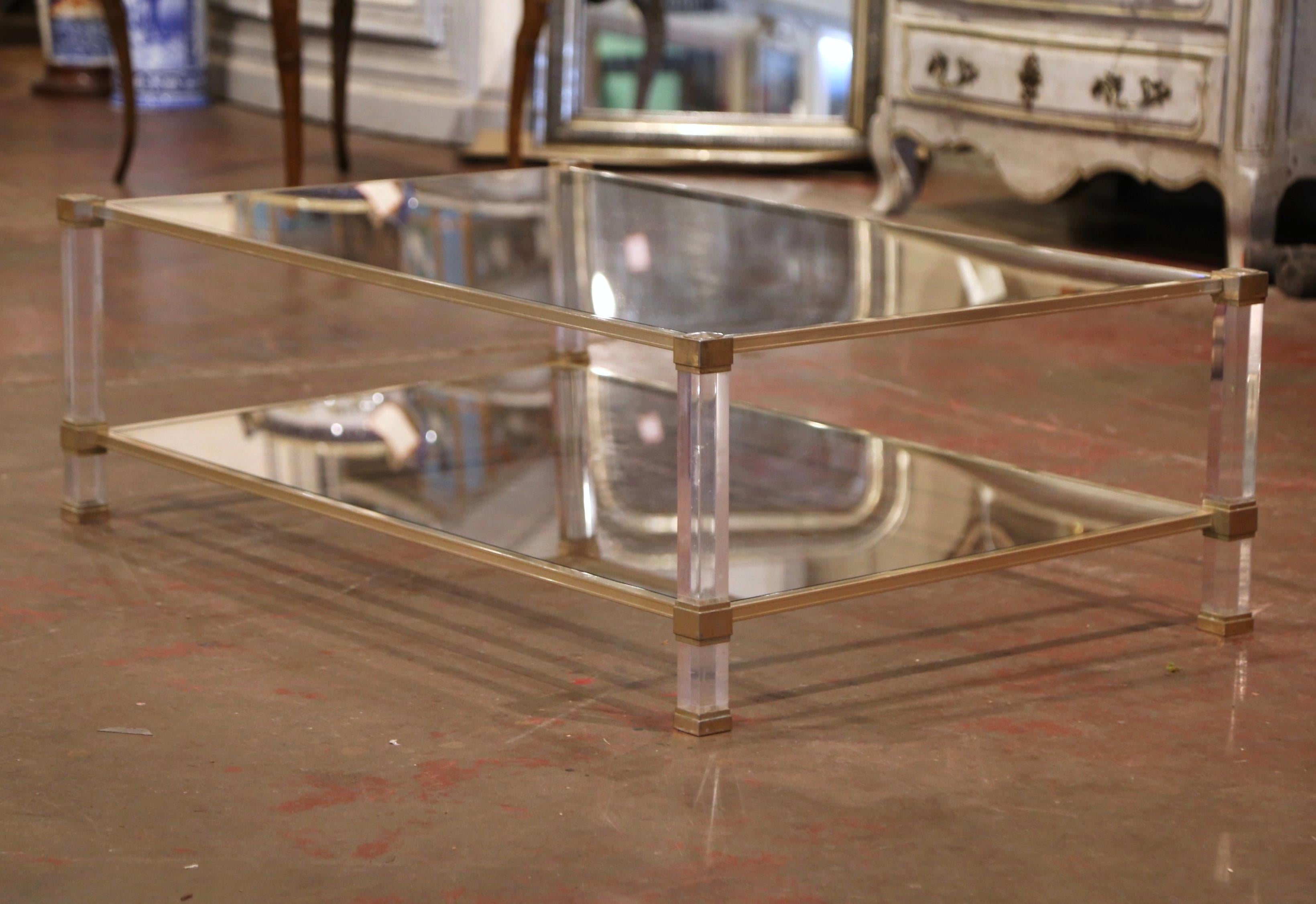 Crafted in France circa 1970 and attributed to Pierre Vandel, the rectangular table stands on four square clear plexiglass legs over a gilt metal frame. The top and the bottom shelf are dressed with inset clear glass surfaces. The elegant two-tier
