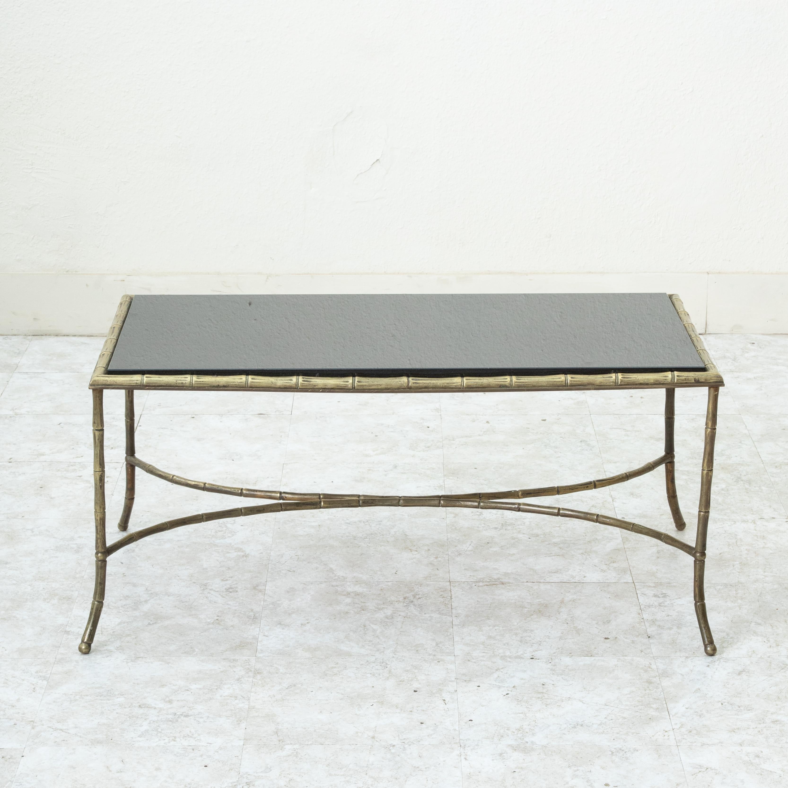 Cette table basse française du milieu du XXe siècle attribuée à la Maison Bagues présente un plateau en marbre noir et un cadre en faux bambou de couleur bronze. Le plateau repose sur des pieds légèrement incurvés reliés par un châssis inférieur