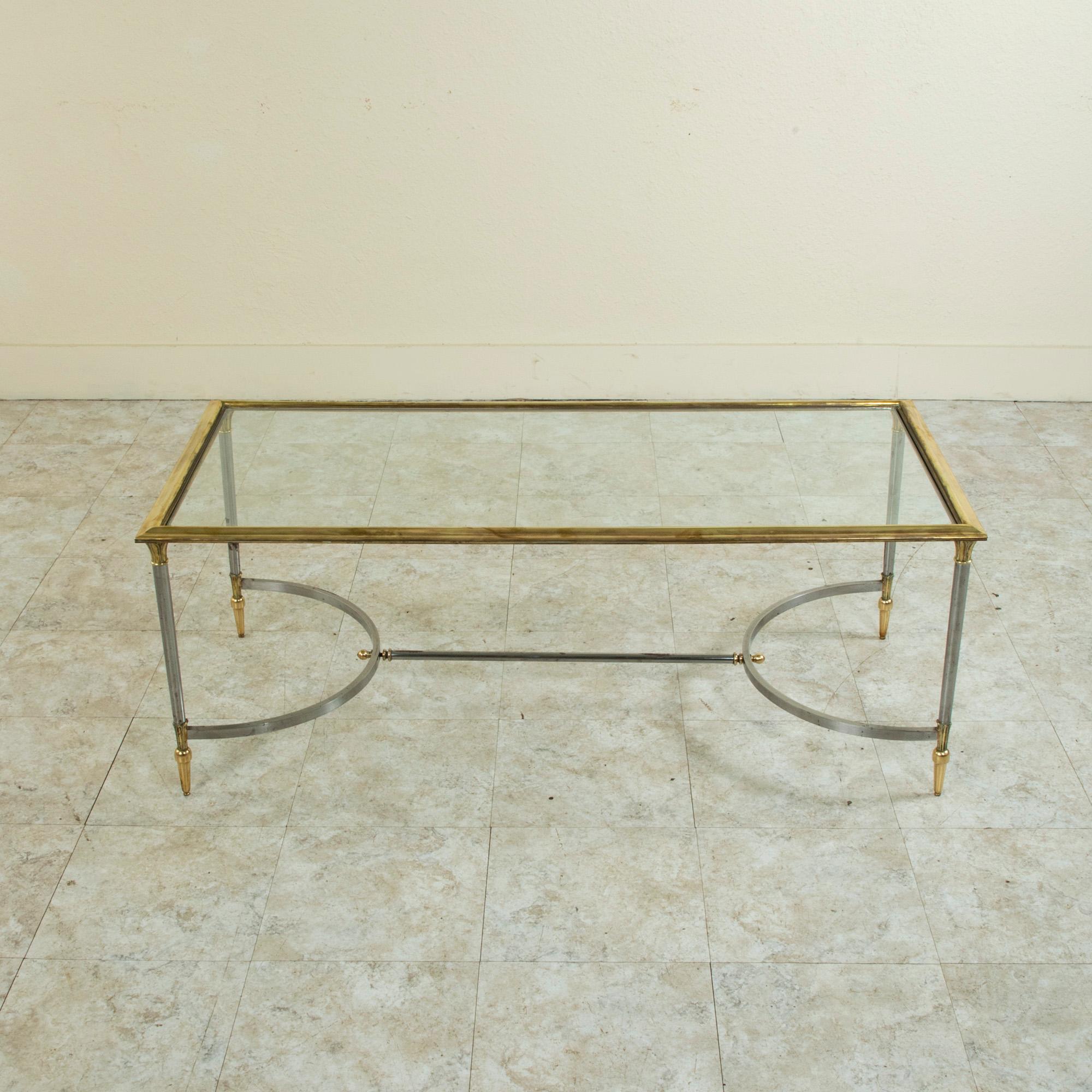 This mid-century French steel and brass coffee table or cocktail table is attributed to the Paris design house Maison Jansen and is inspired by the Directoire style with its Egyptian style capitals at the top of each leg. The base is joined by an H