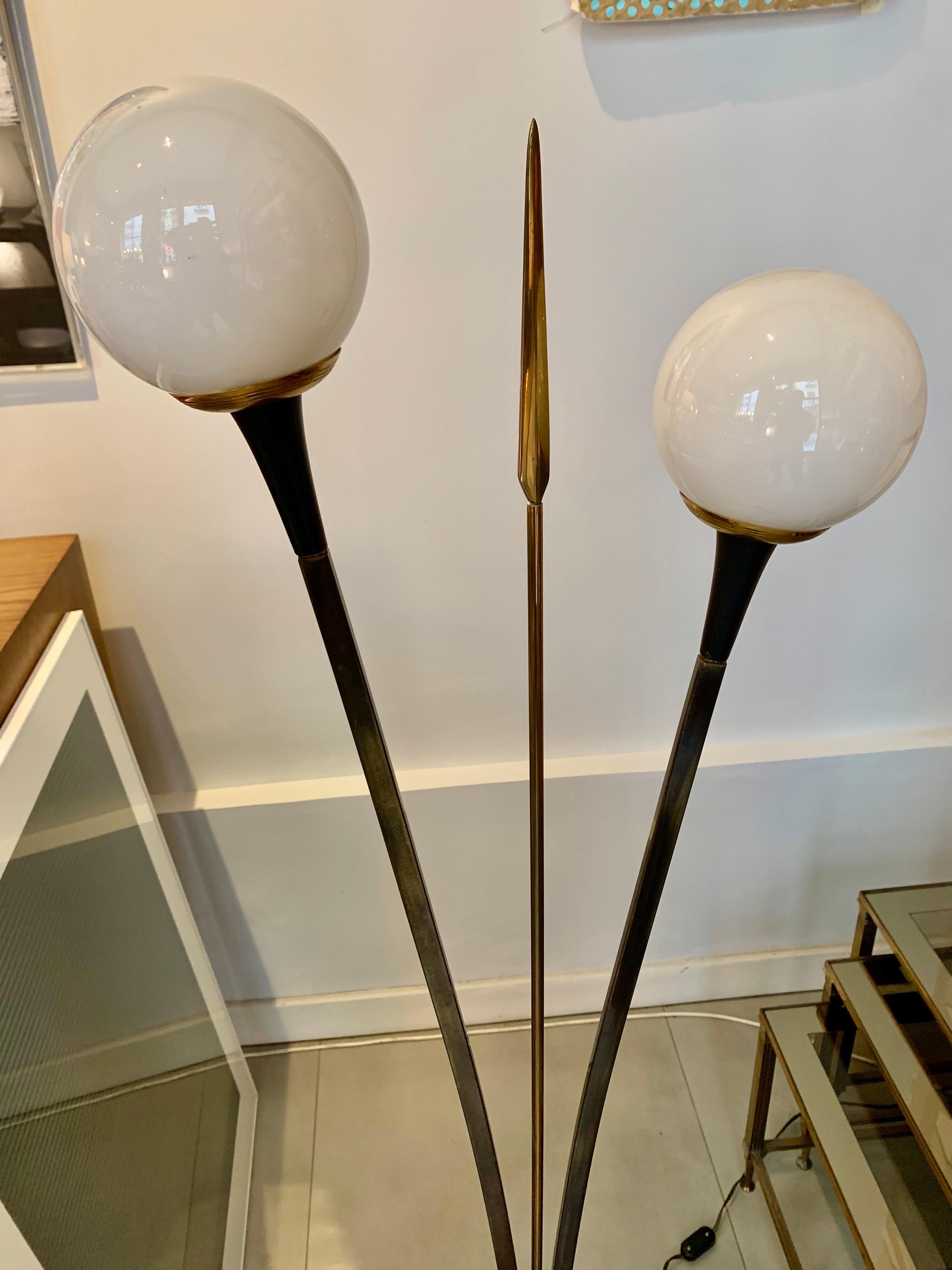 Lamp from the early 1960s, by the French Maison Lunel, the lamp consists of three columns, two of which end in a circular white opline lampshade and the other with a glass ornament, it is made of gilded brass and lacquered metal. Its electrical