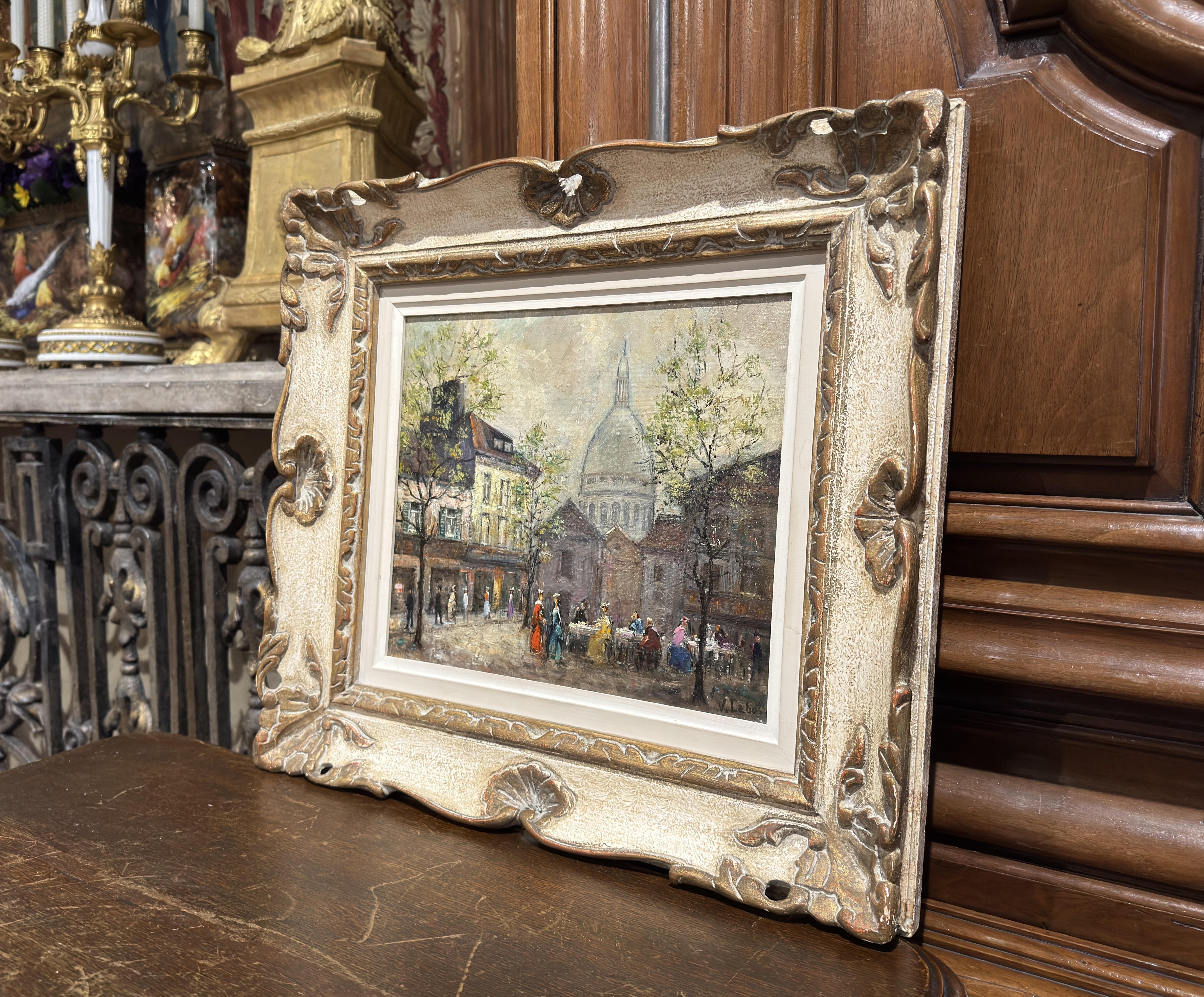 Decorate a den or office with this exquisite Parisian street oil painting. Created in Paris, France circa 1950, this artwork is beautifully set in a carved antique two-tone cream and gold frame. The canvas, signed by French artist V. Lebot in the