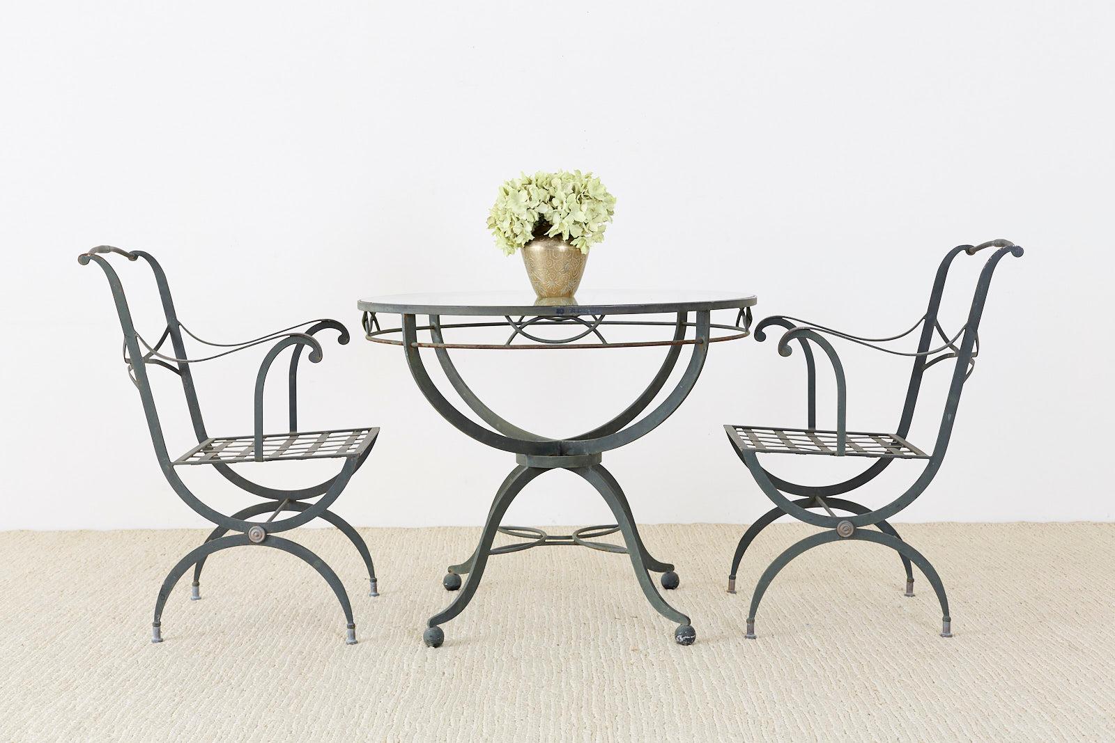 Unique Mid-Century Modern French garden or patio dining table constructed from iron with a beautiful patinated metal finish. The round top is inset with a pane of glass and a decorative apron. The graceful legs are conjoined in the middle with a
