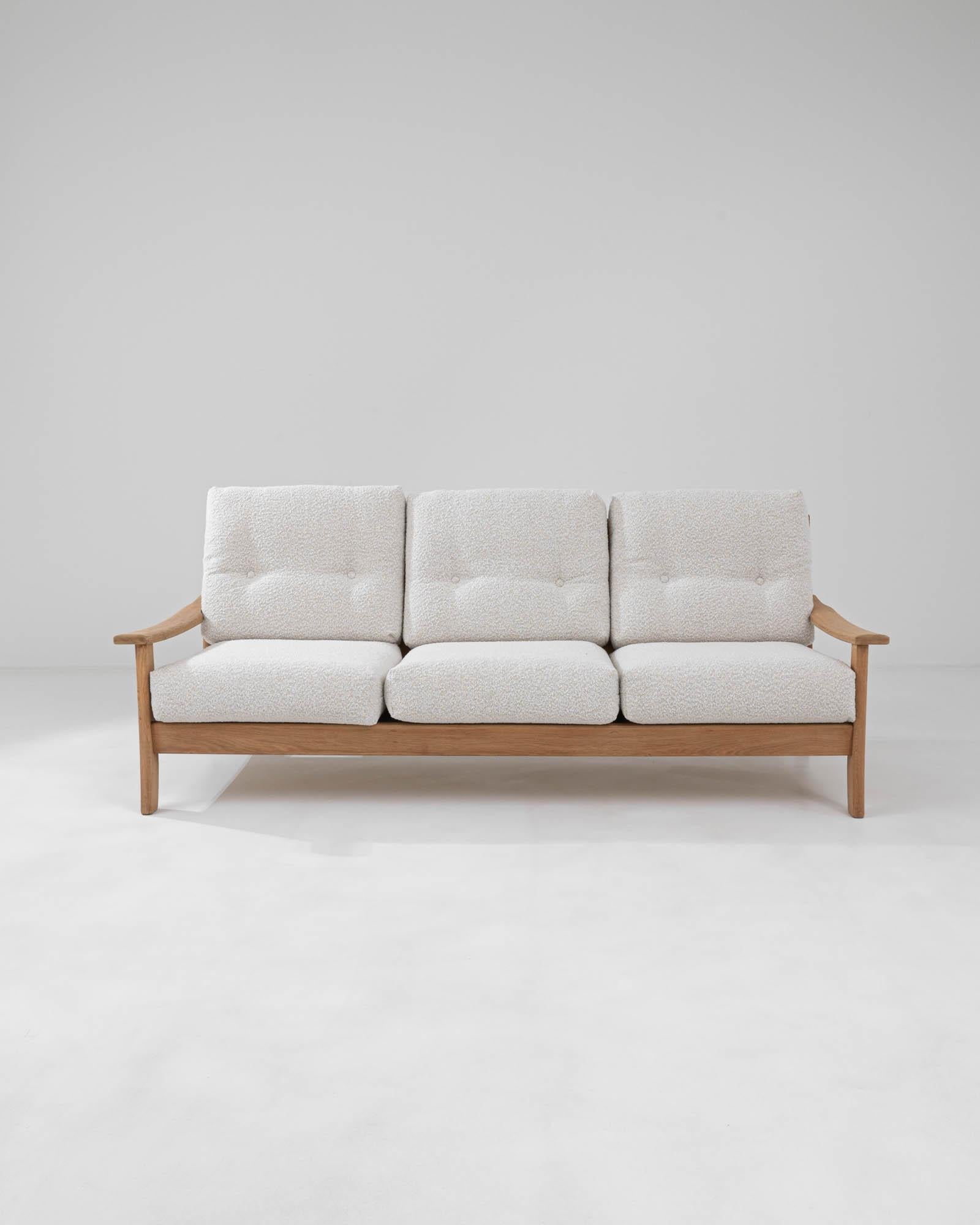 An oak three-seater sofa made in mid-20th century France. Dynamic shapes and a homey natural color palette make an effortlessly elegant impression. Warm oak with a natural finish is fashioned into a light frame; the repeated curved back-slats create