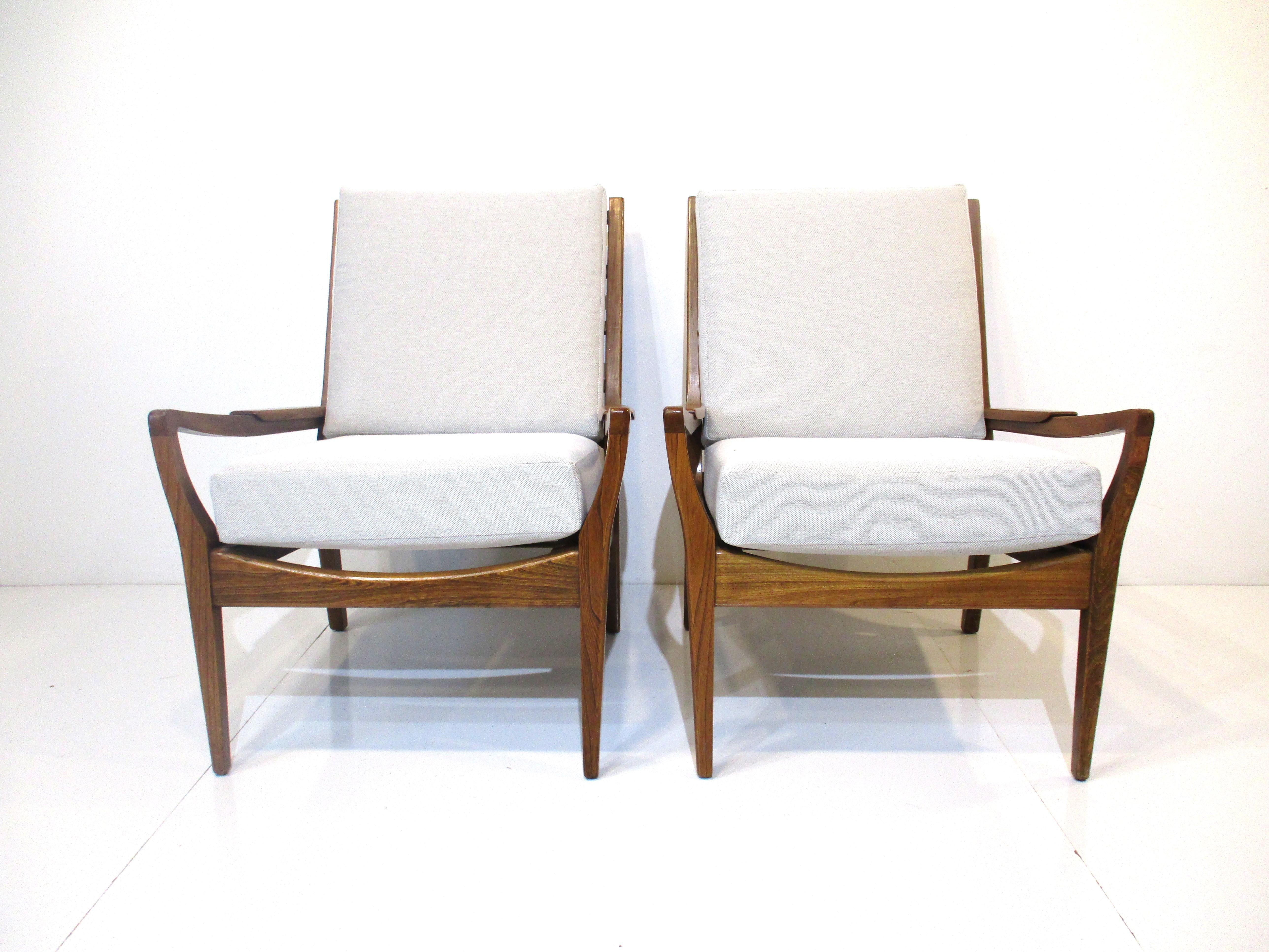 A pair of very well crafted and sturdy wood framed lounge chairs each with two loose upholstered cushions in a woven taupe and cream contract fabric. Designed having a laid back profile and small matching wood arm pads for comfort and wood slat