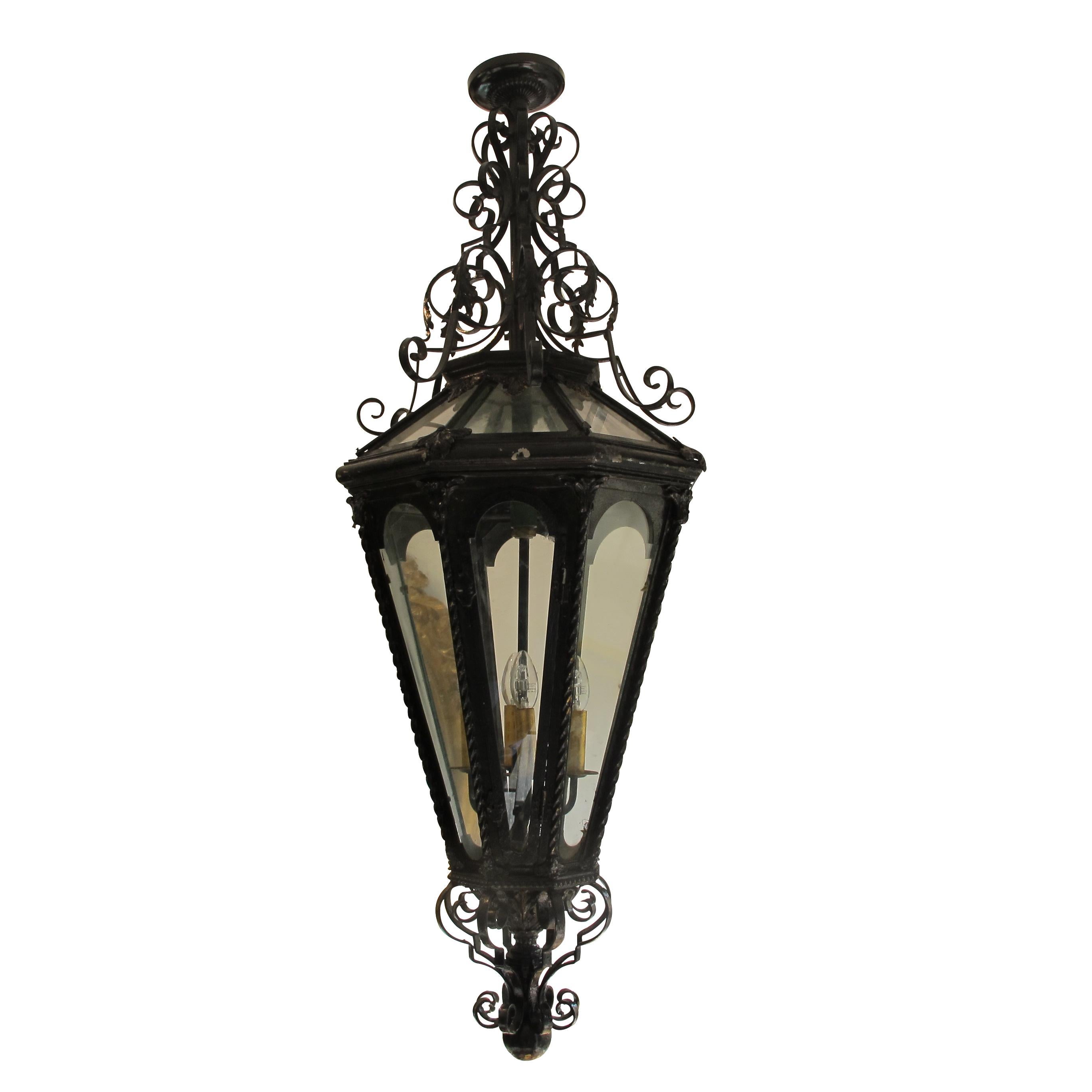 This is a very large black-painted wrought iron French lantern circa 1950s. The lantern holds 4 light fittings accessible through one of the facet-mounted door. The lantern is highly decorative with ample forged scrolls with generous curves and