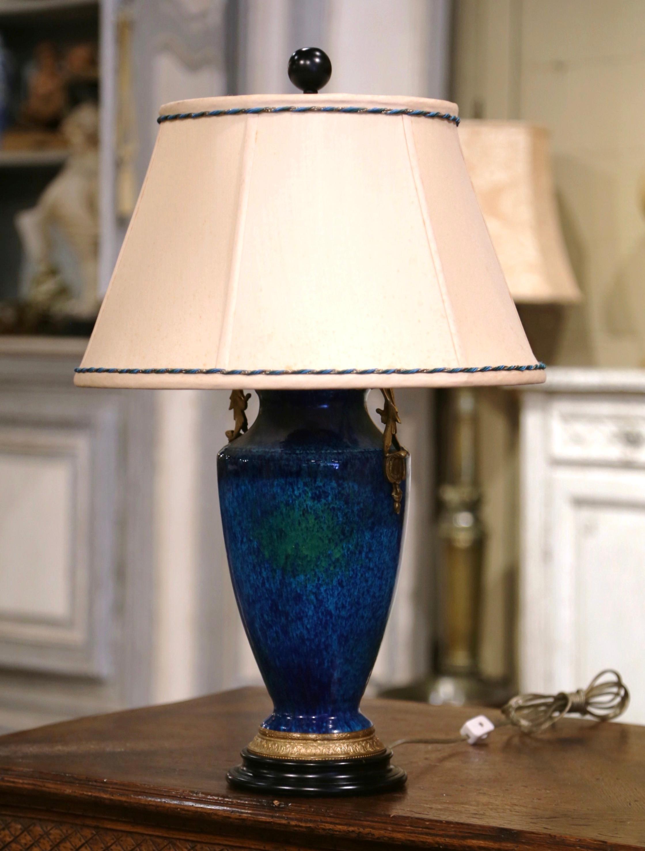 Add the perfect blue accent to your home with this colorful porcelain urn lamp. Crafted in France circa 1950, the ceramic vase stands on a circular wooden base and is accented with elegant bronze handles and a decorative carved bronze ring at the