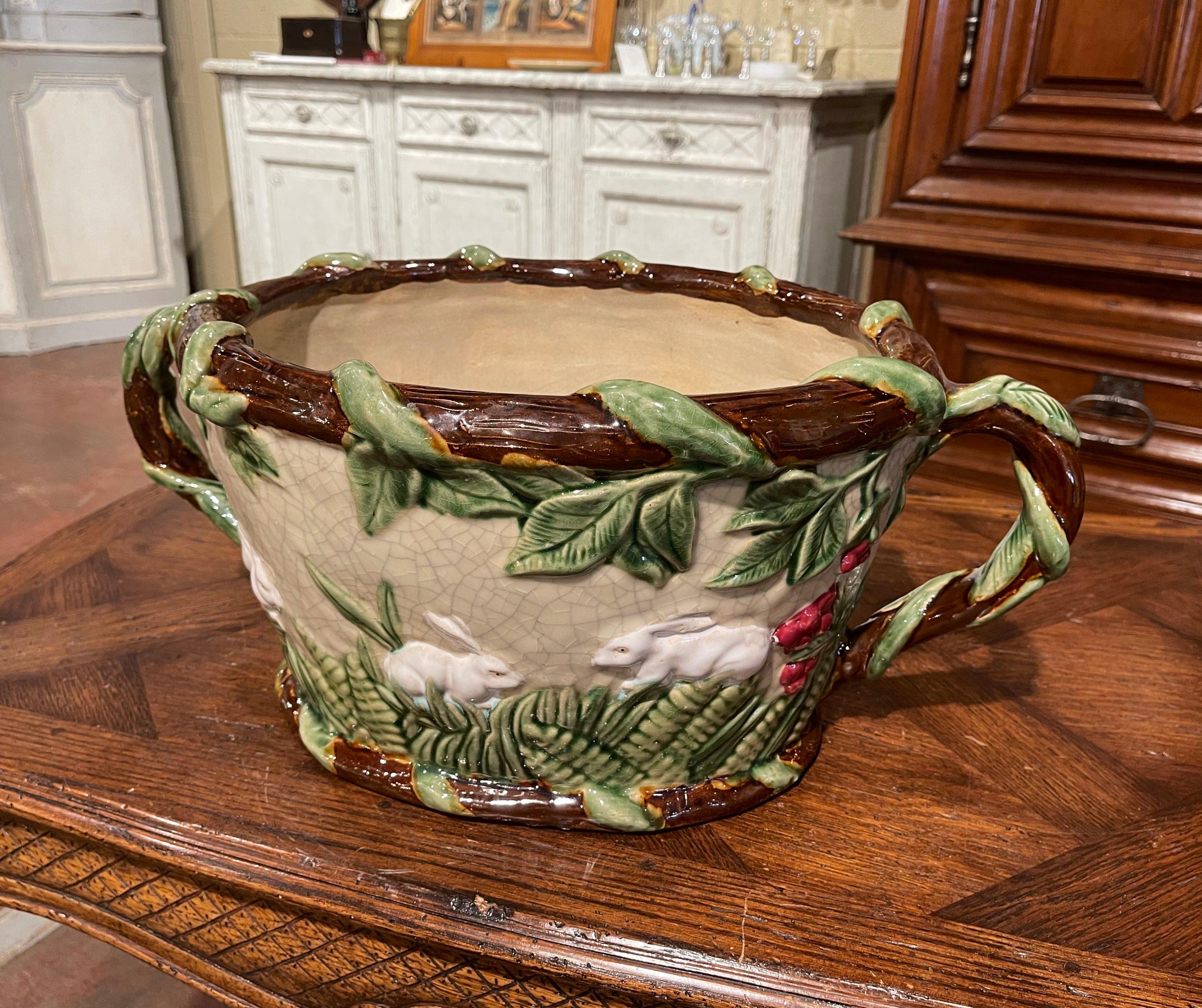 This colorful antique barbotine jardinière was sculpted in France circa 1960. Oval in shape with elegant twisted tree form handles, the antique porcelain cache pot features exquisitely rendered rabbit and foliage motifs in high relief. The large