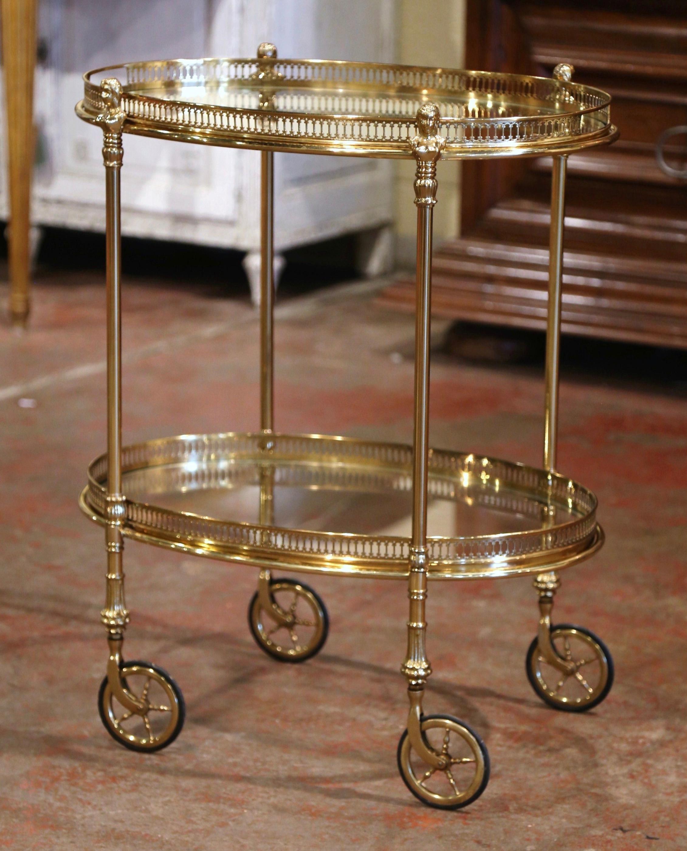 This beautiful, vintage two-tier rolling bar cart was created in France, circa 1950. Built in brass and oval in shape, the dessert table stands on small round wheels with rubber tires, over two plateaus topped with glass surfaces. The top deck