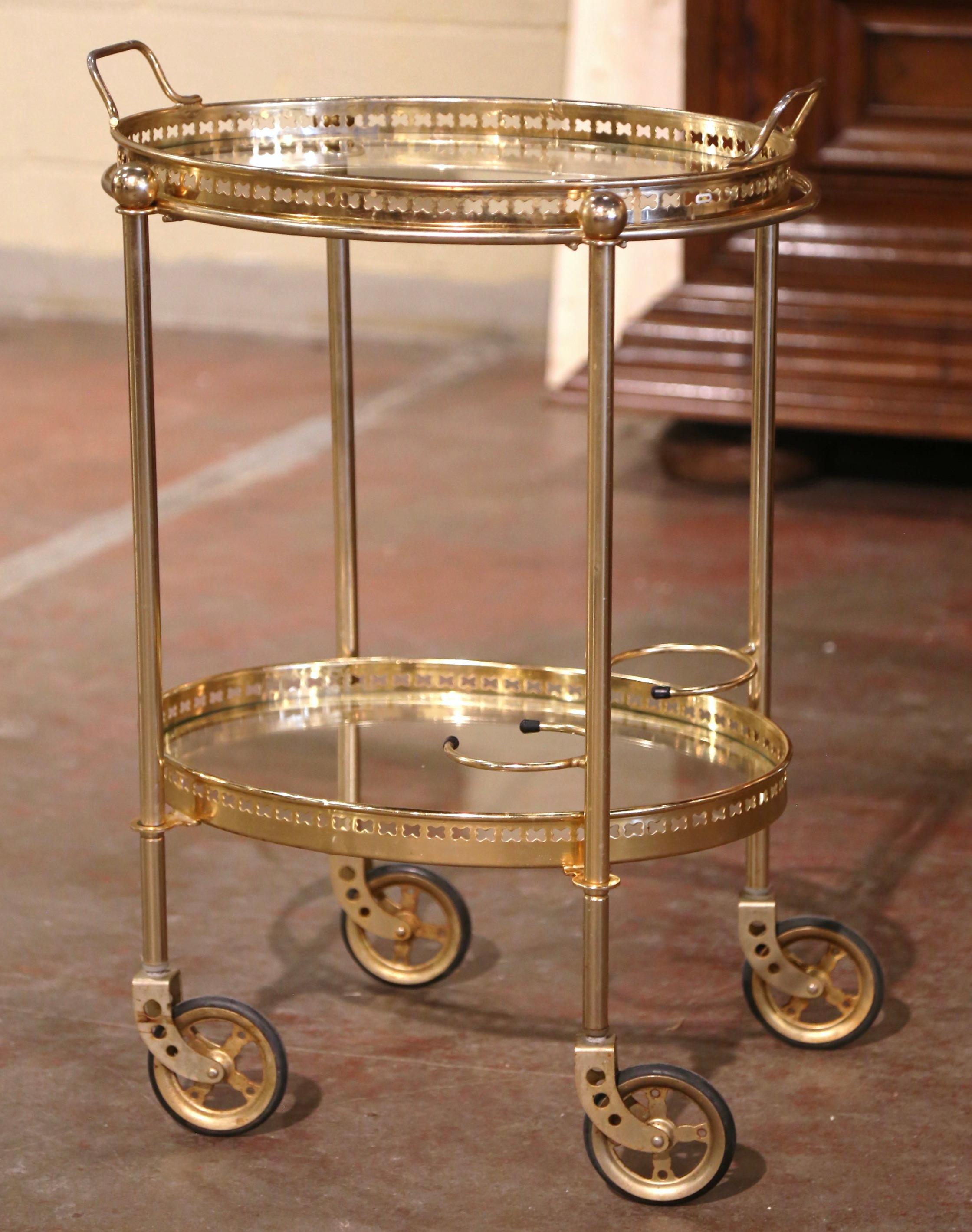This elegant vintage rolling bar cart was created in France, circa 1960. Built in brass and oval in shape, the two-tier dessert table stands on small round wheels with rubber tires, over two plateaus topped with glass surfaces. The top deck features