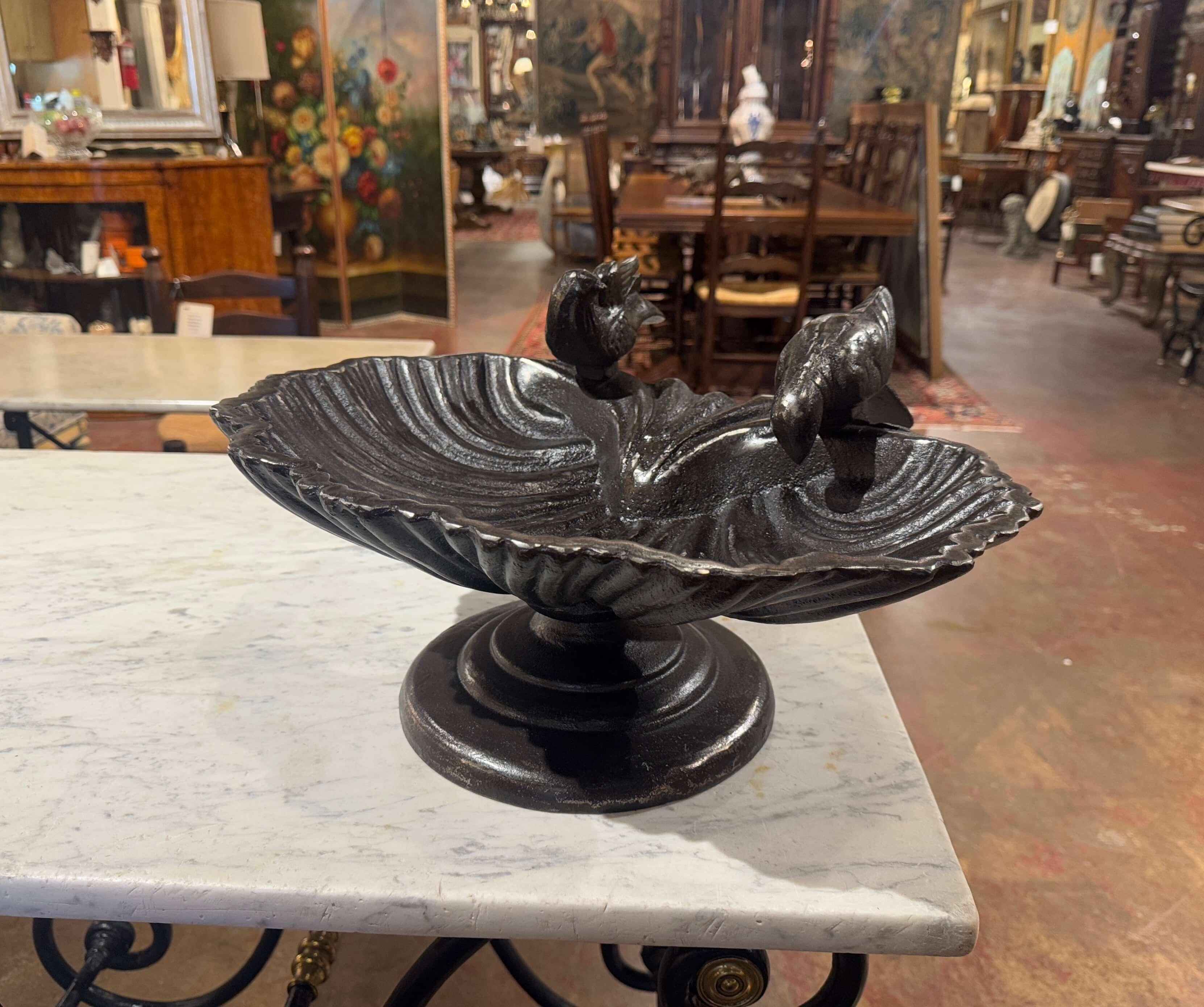 Décorez votre jardin avec ce lourd bain d'oiseaux antique. Fabriqué en France vers 1950, le plat en fer repose sur un socle circulaire robuste qui lui confère une grande stabilité. Il présente un bassin festonné, semblable à un coquillage, avec des