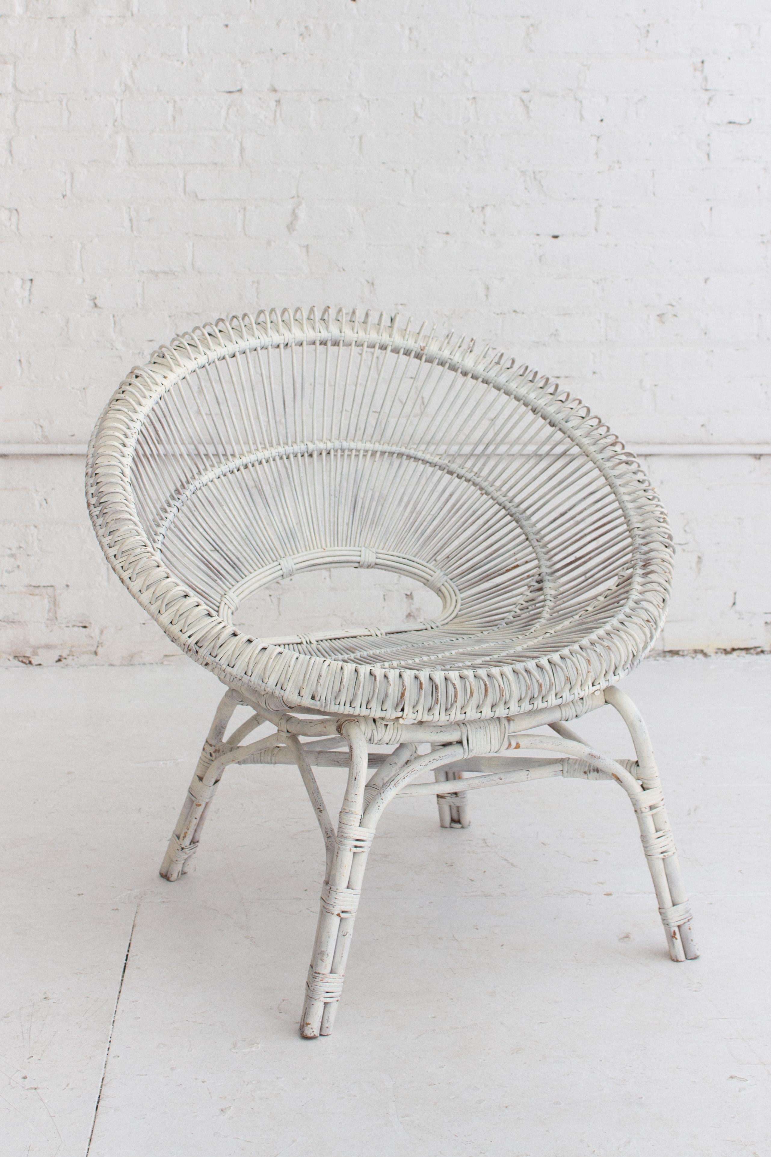 A midcentury French rattan chair. Circular Silhouette. White paint has chipped and patinaed with age.