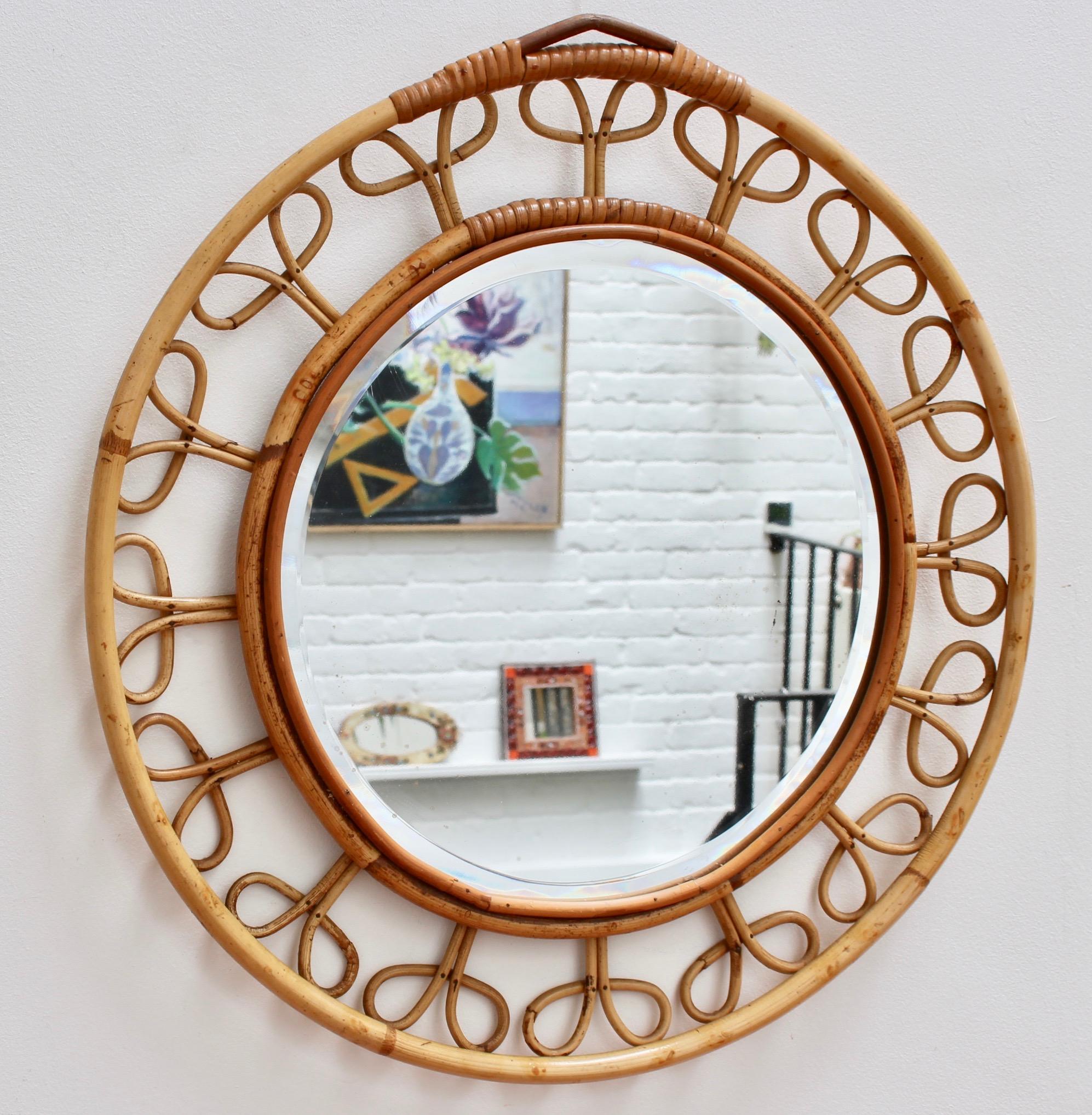 Midcentury French rattan round wall mirror (circa 1960s). This vintage mirror is formed by two concentric circles framing the glass. They are connected by sixteen rattan flower motif designs creating a chic and appealing piece. This is a very rare