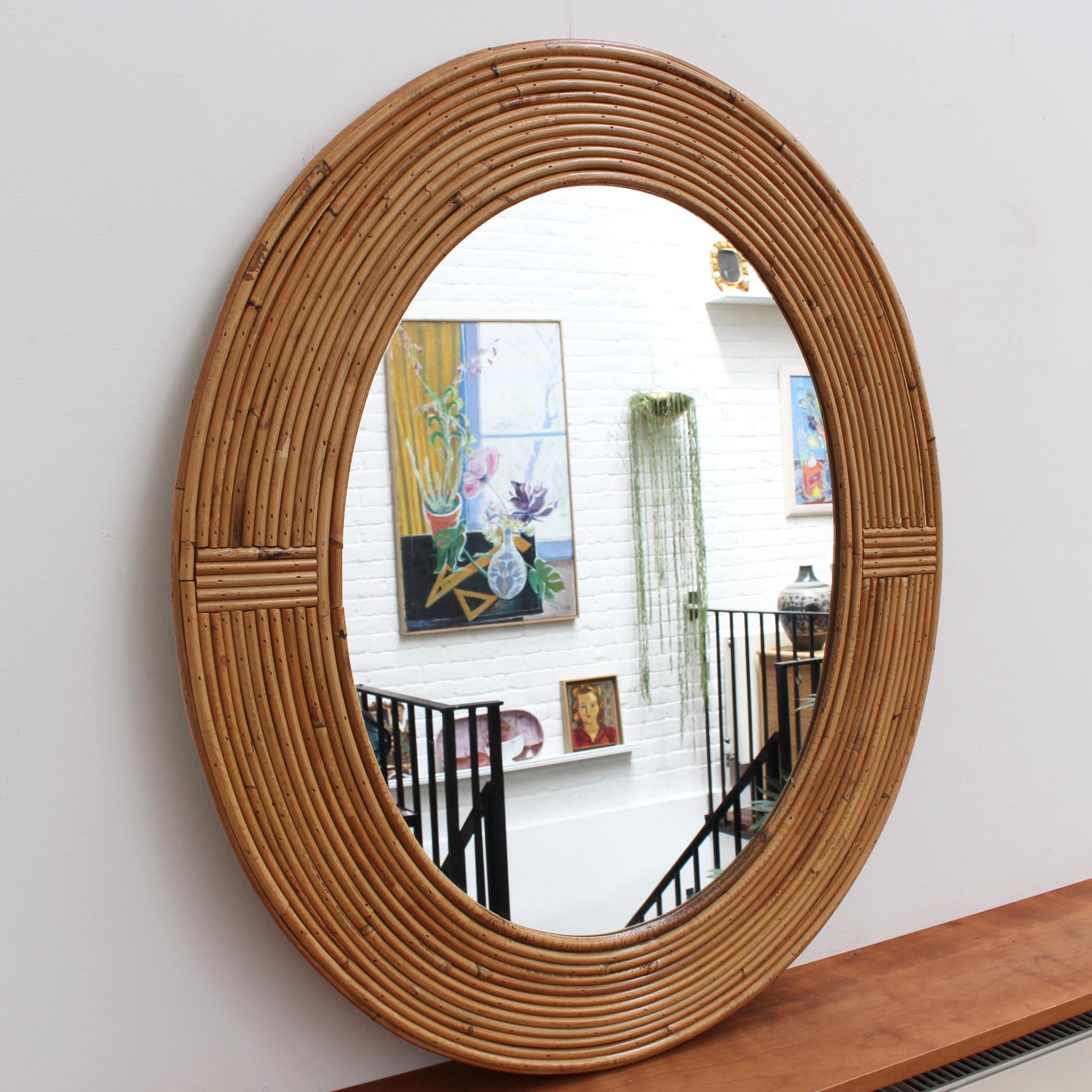 Vintage French rattan wall mirror circa 1960s. A dozen concentric tubular rounds of rattan form the structural frame for this stunning oval mirror. The circles are punctuated at the sides / top (depending on how you choose to hang it) by horizontal