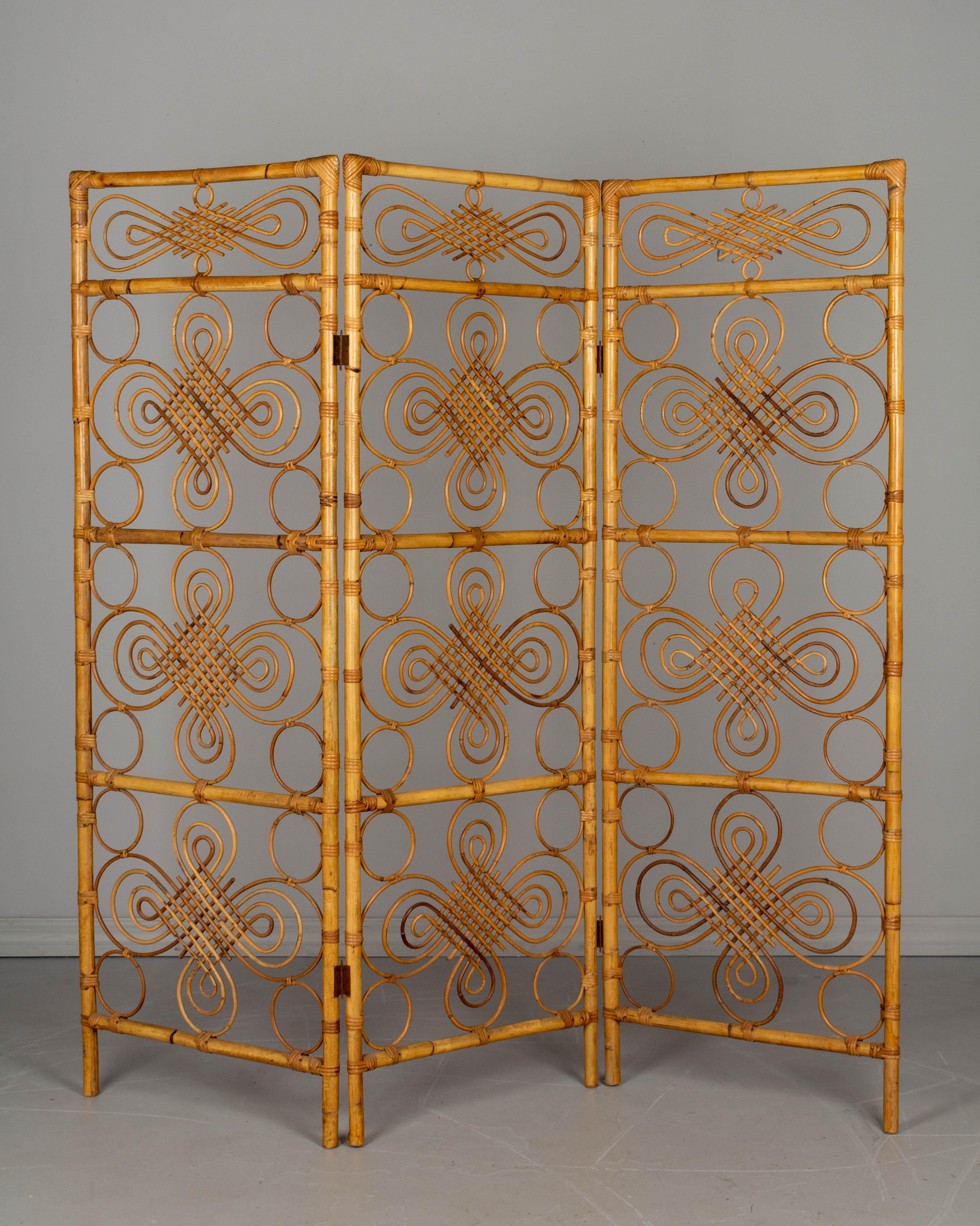 A midcentury French Riviera three-panel folding screen, or room divider, with sturdy handcrafted bamboo and rattan frame and wicker filigree decoration. Brass-plated hinges. Each panel is 1.25