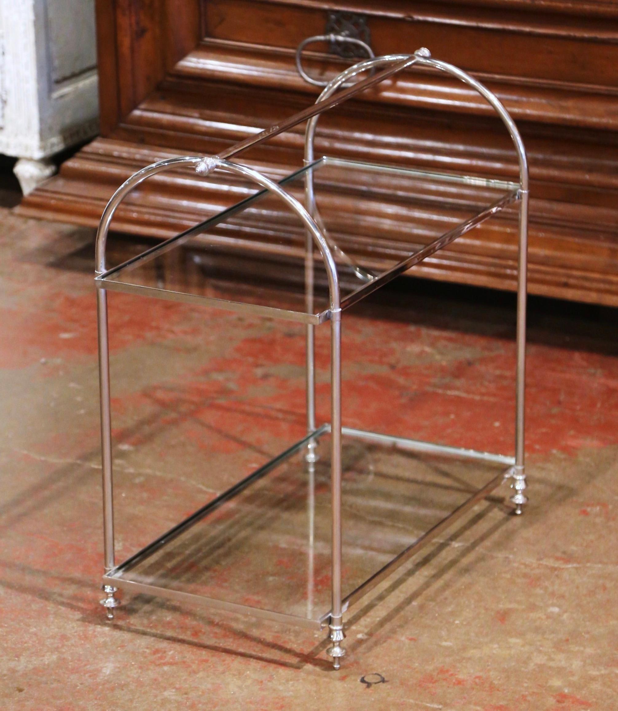 Crafted in France circa 1930, the art deco serving table stands on straight legs ending with toupie feet; ithe table features a large handle over two arched supports across the top. The antique display bar cart is dressed with two colorless glass