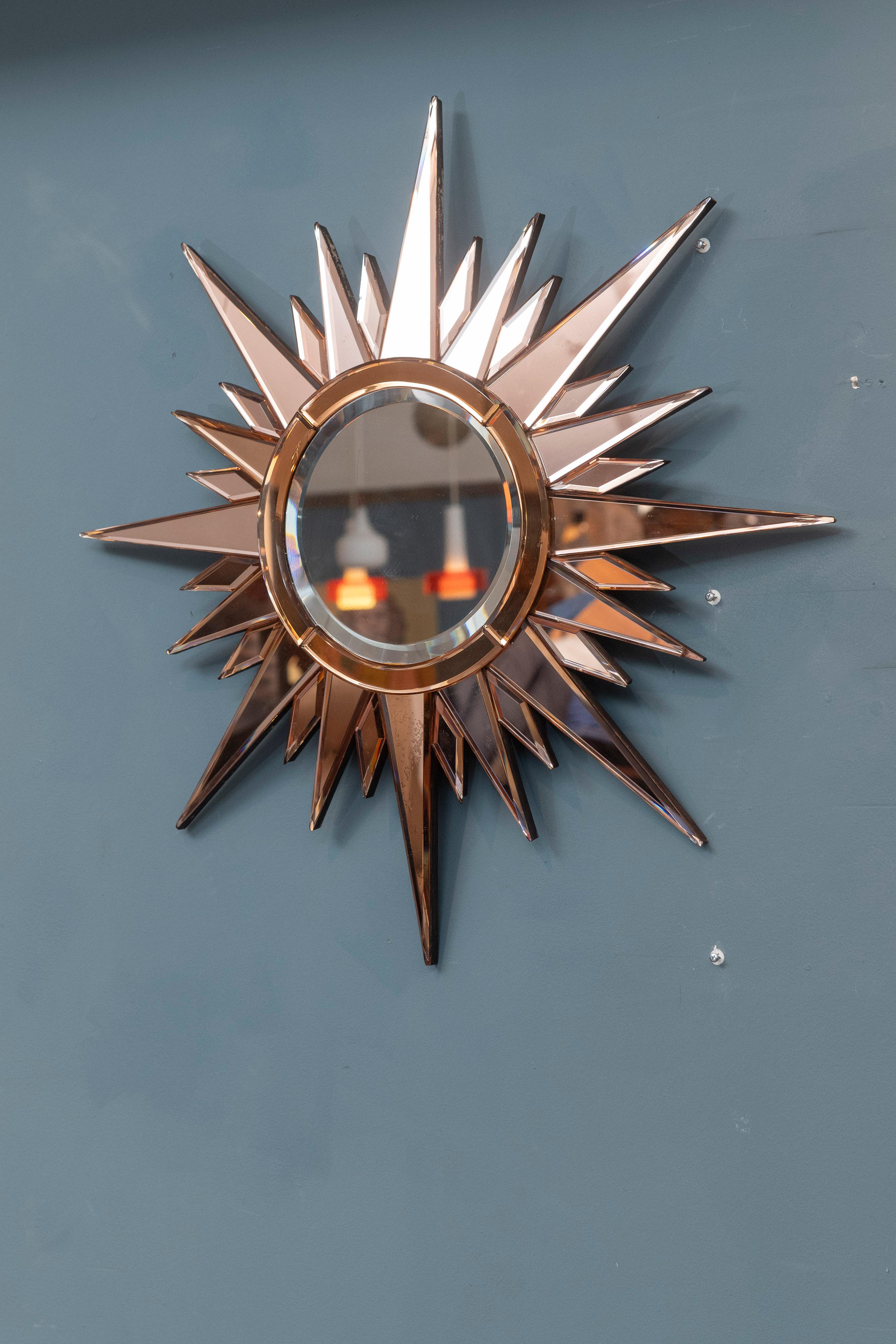 Mid-Century French starburst wall mirror. Peach glass with beveled edges throughout and a clear mirror center. Eye catching design and unusual color that will add glamour to any room. Age appropriate wear with signs of age with one small tip chip as