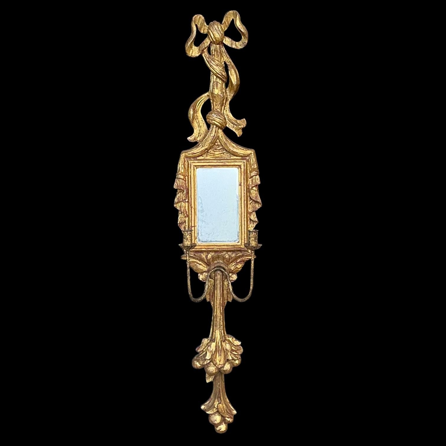 This is a carved giltwood sconce with French styling. It was hand crafted in Spain during the 1960s. It has two candle holders and a petite mirror. The elaborately carved ribbon is in very good condition. 