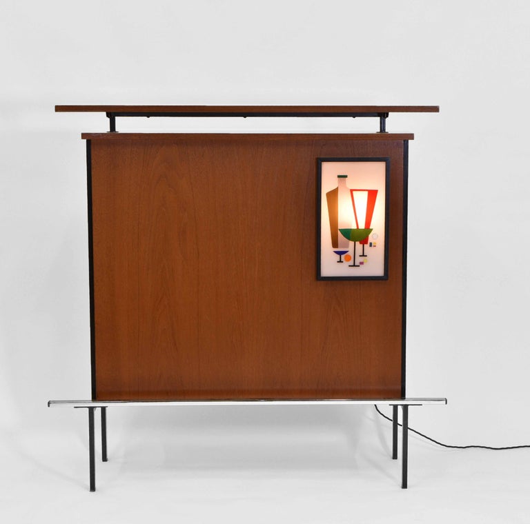 A very stylish Mid-Century French teak and blackened metal framed cocktail drinks bar with chromed footrest. Circa 1960.

The bar has a fabulous multi-coloured Perspex illuminated panel depicting a cocktail drinks arrangement, with an ebonised