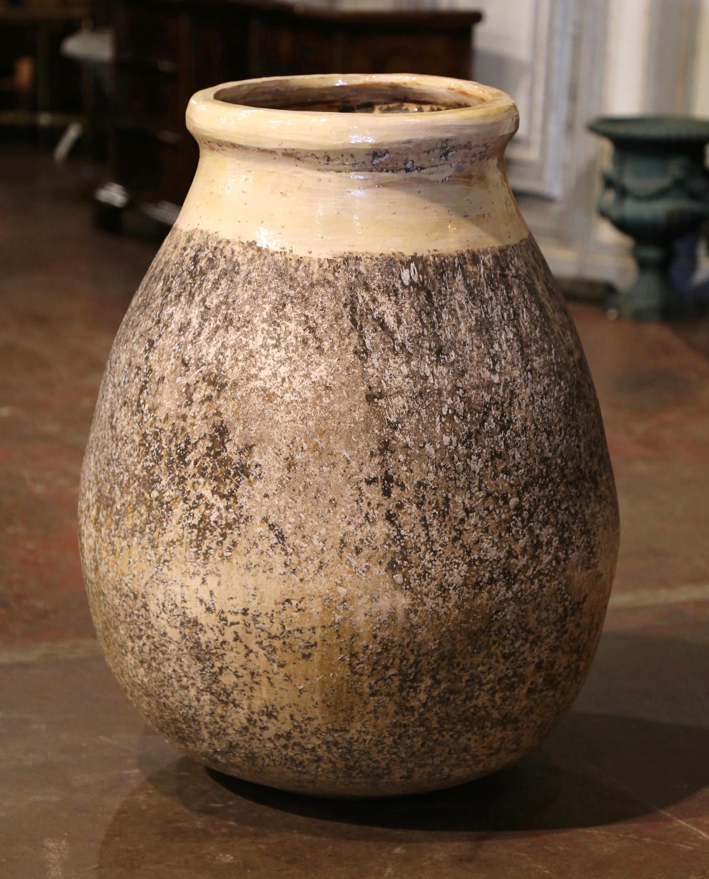 This large, antique earthenware olive jar was created in Biot, Southern France, circa 1970. Made of blond clay and neutral in color, the terracotta vase has a traditional round bulbous shape. The rustic, time-worn pot features a pale ochre glaze