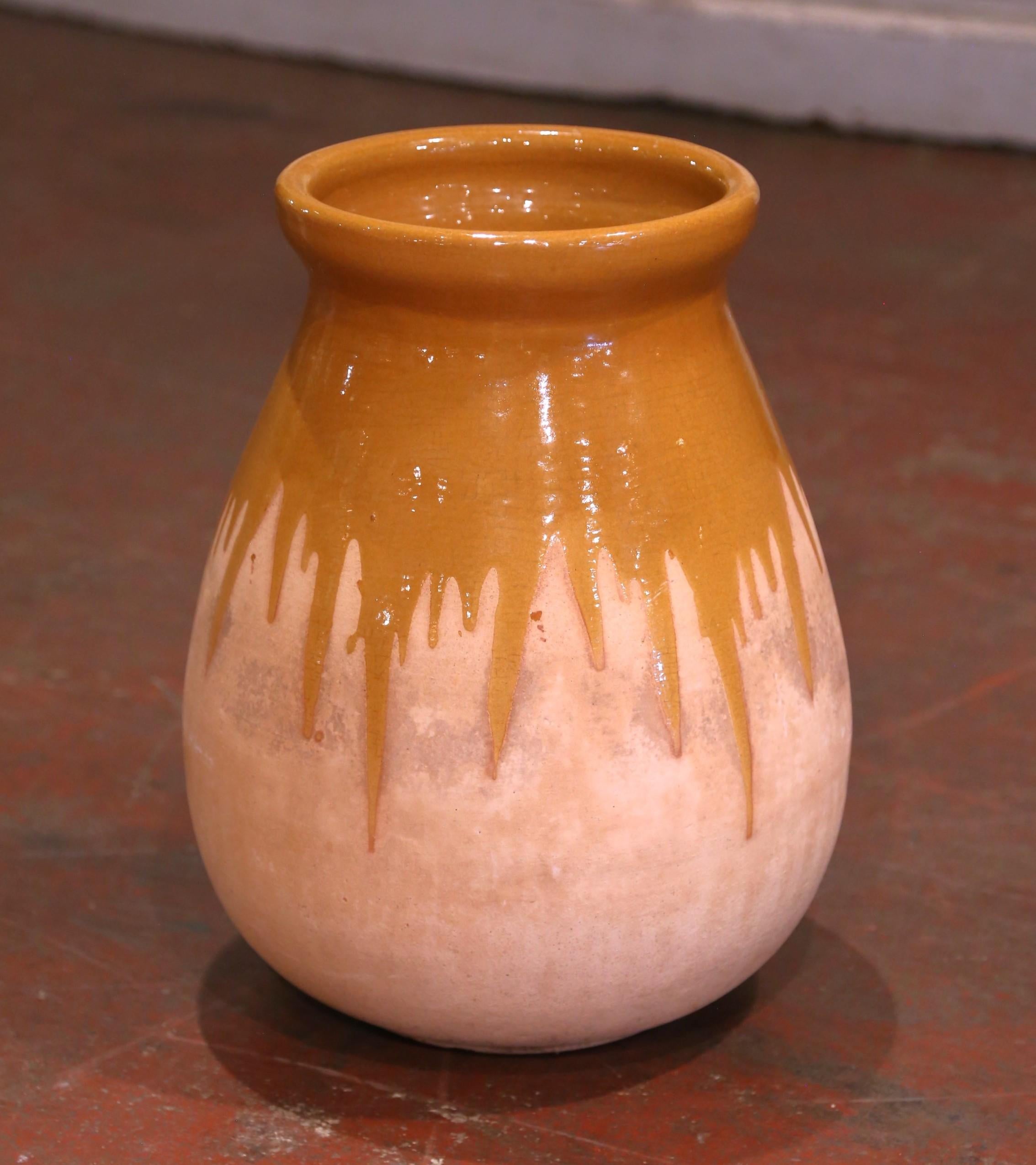 Cette ancienne jarre à huile d'olive en faïence a été créée dans le sud de la France, vers 1970. Fabriqué en argile blonde, le vase en terre cuite a une forme ronde traditionnelle. Ce pot rustique et usé par le temps présente une glaçure orange