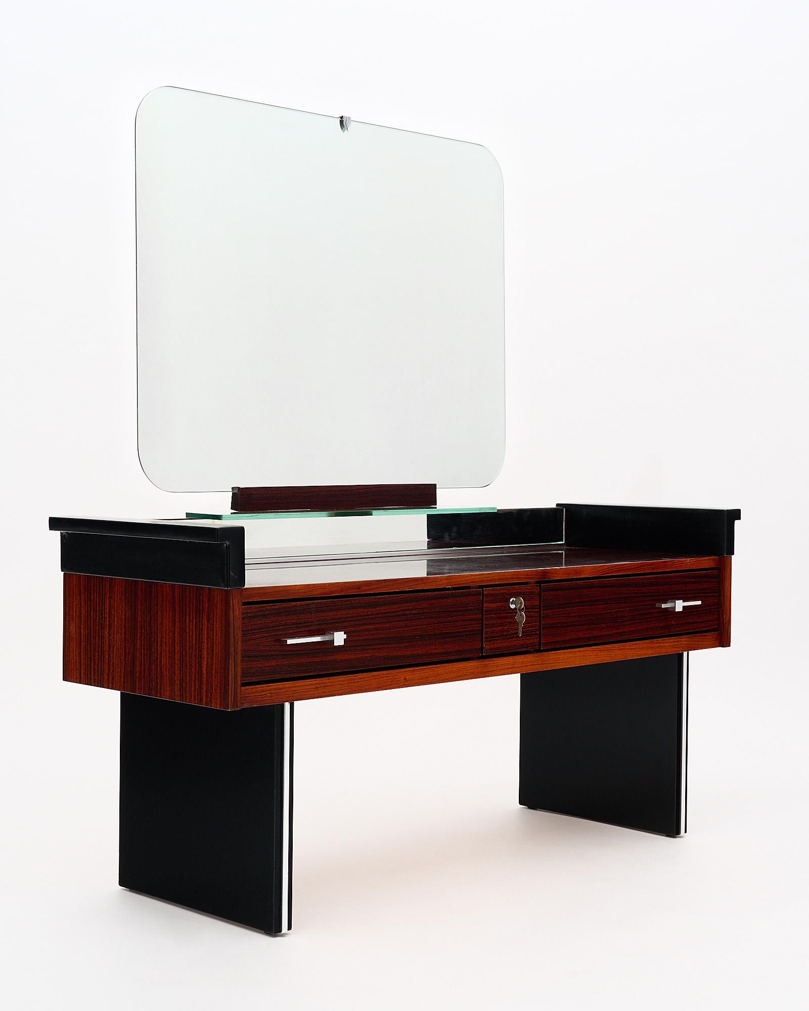 Vanity, French, made of rosewood and ebonized mahogany. The table features vinyl sides and the original mirror. The mirror itself is 27.25” in height and 32” in length. The height to the top of the vanity is 21”. There are three drawers, the central