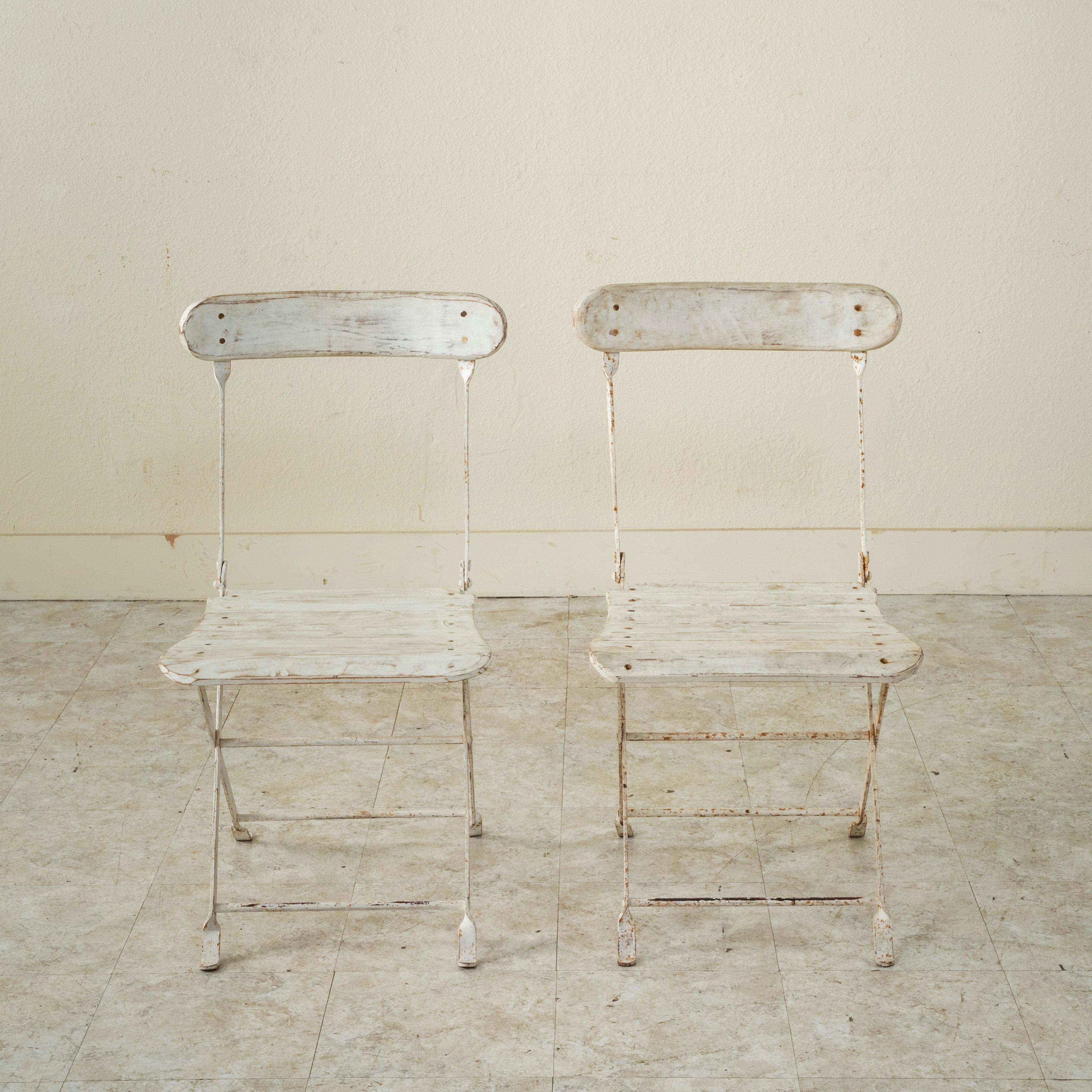 This pair of Mid-twentieth Century French iron garden chairs feature wood slats on the seats and backs and are painted white. The chairs fold flat for easy storing, circa 1950. Five pairs available.