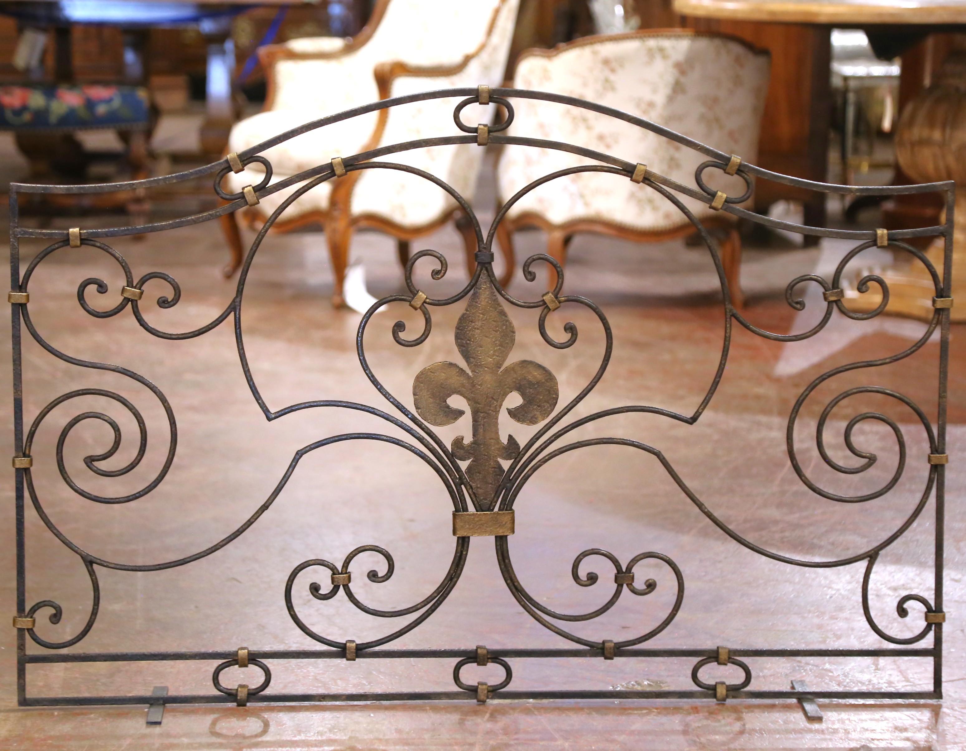Hand-forged in France circa 1960, this elegant vintage screen features a scrolling wrought iron frame centered by a boldly stylized fleur-de-lis motif. The symmetrical design is composed of fluid, curving volutes that radiate outward in a rhythmic