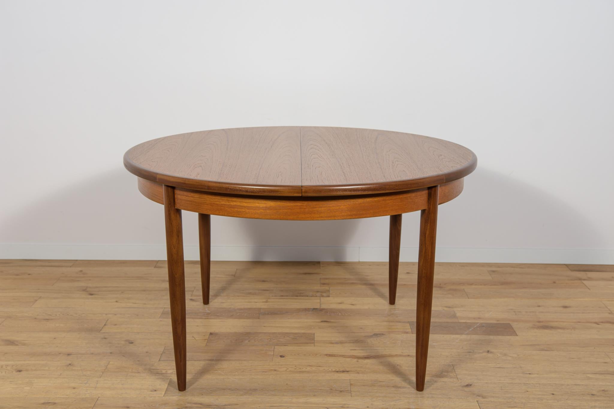 Esta mesa de comedor redonda extensible fue fabricada por G-Plan en la década de 1960. La mesa tiene los bordes de la parte superior perfilados y reforzados. Elementos de teca limpiados de revestimiento antiguo y pintados con tinte de roble y