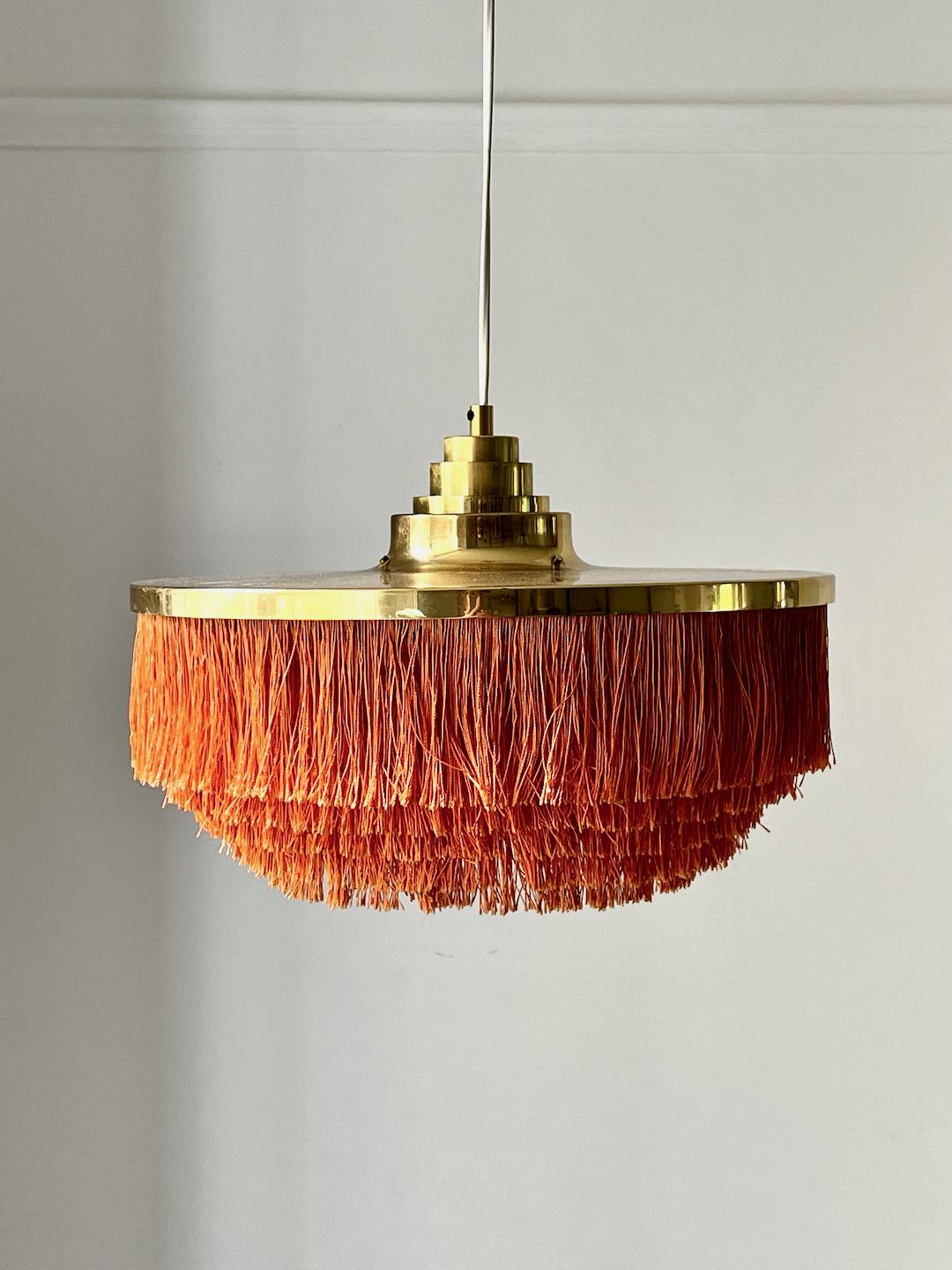 Pendant light by the Swedish designer Hans Agne Jakobsson for his own company in Markaryd. A very nice piece of Scandinavian modern design with aged patina. Labelled.

Large brass canopy with stepped detail and layered fringes in orange silk. Brass