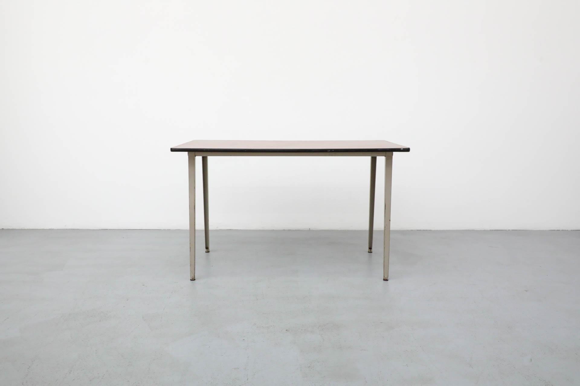 Table de réforme épurée du milieu du siècle, conçue par Friso Kramer pour Ahrend Circle en 1955.  Structure industrielle en métal gris émaillé avec plateau en Formica en faux bois de teck. Un style si emblématique que le Stedelijk Museum d'Amsterdam