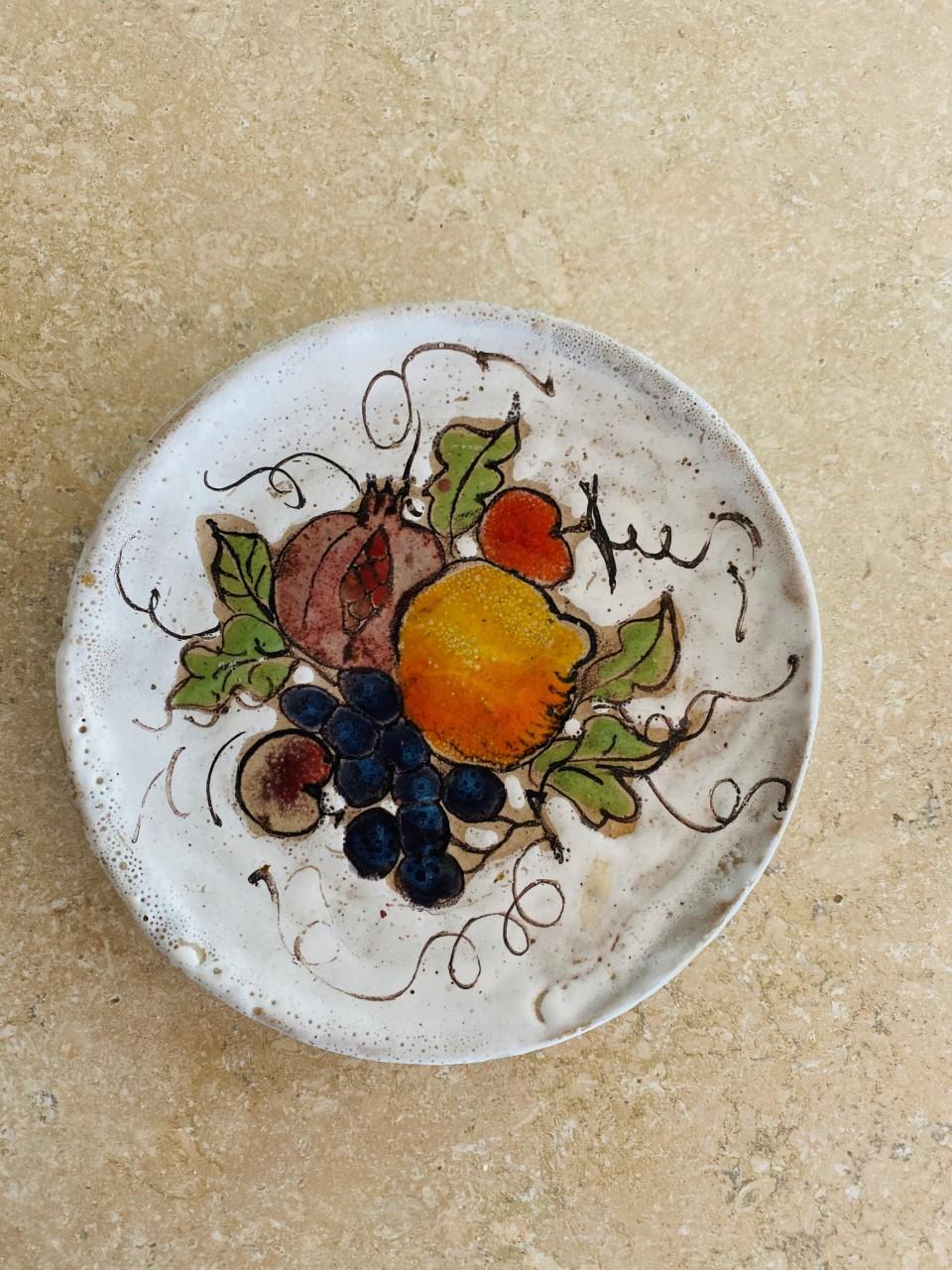 Belle assiette en céramique peinte à la main avec une nature morte de fruits par Elios Schiavon. Cette pièce du milieu du siècle est pleine de détails : Schiavone représente une nature morte dans une variété de couleurs vives avec une glaçure