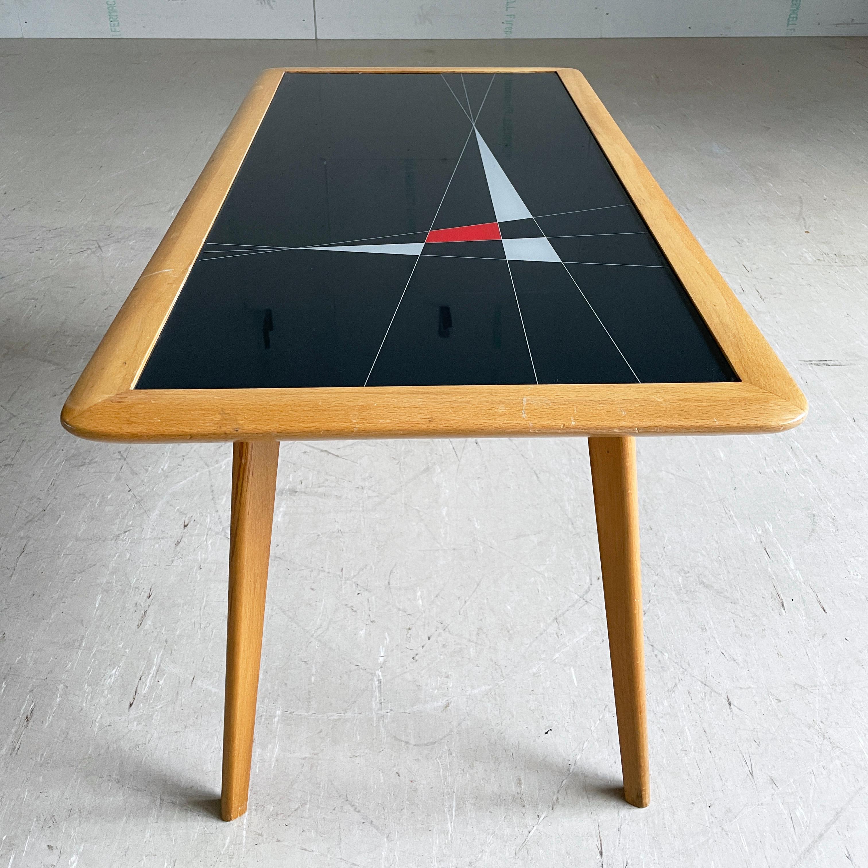 Table basse du milieu du siècle avec un plateau en verre incrusté avec un design atomique stylisé et un entourage et des pieds en bois. Produit par FUBO, Suisse, vers 1950 - 1960.
