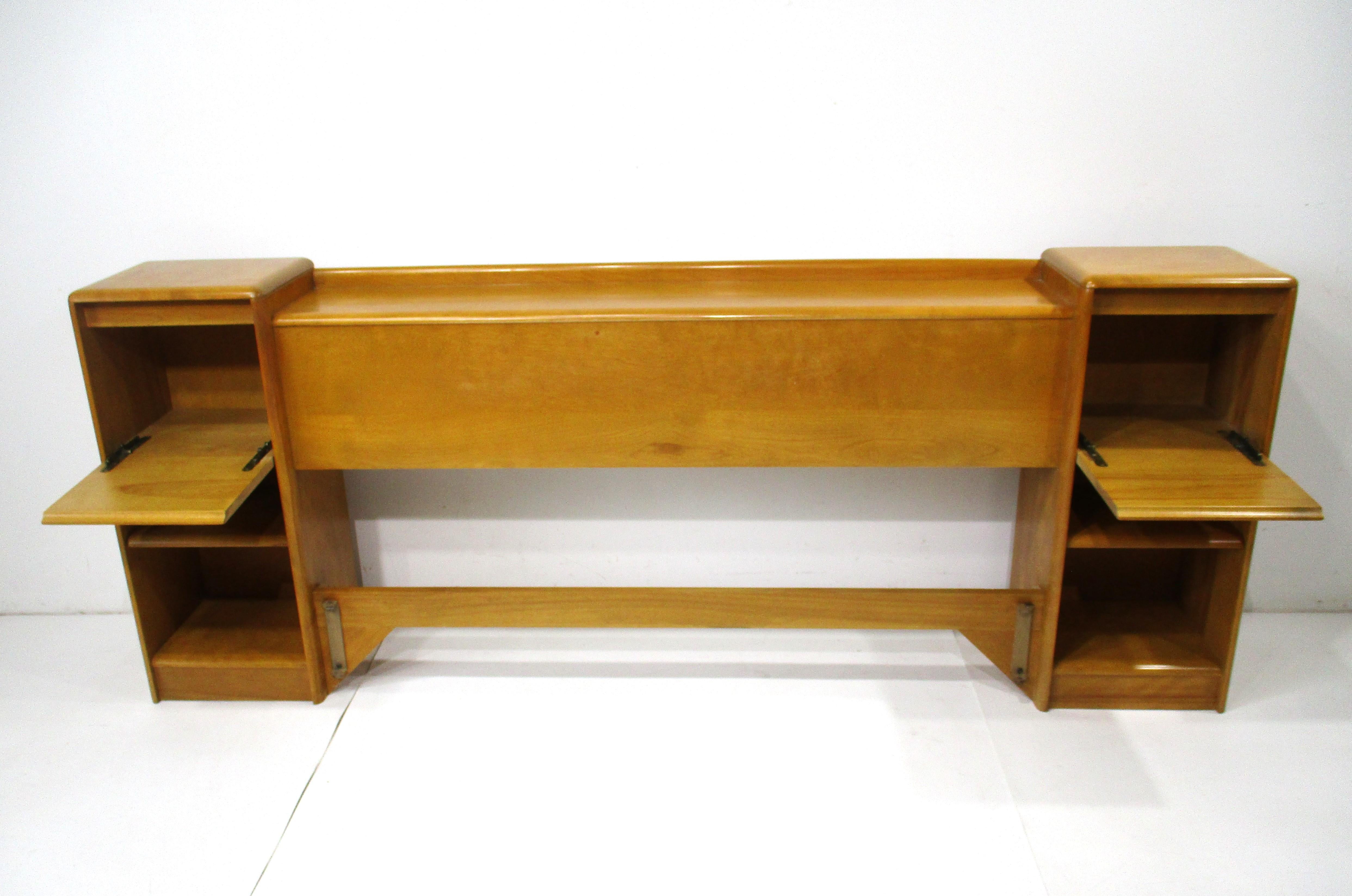 A solid maple full sized headboard with pull down doors that become night tables and storage bins . The lower area has two storage areas to each side with a single adjustable shelve , from the Heywood Wakefield Furniture company designed by Leo