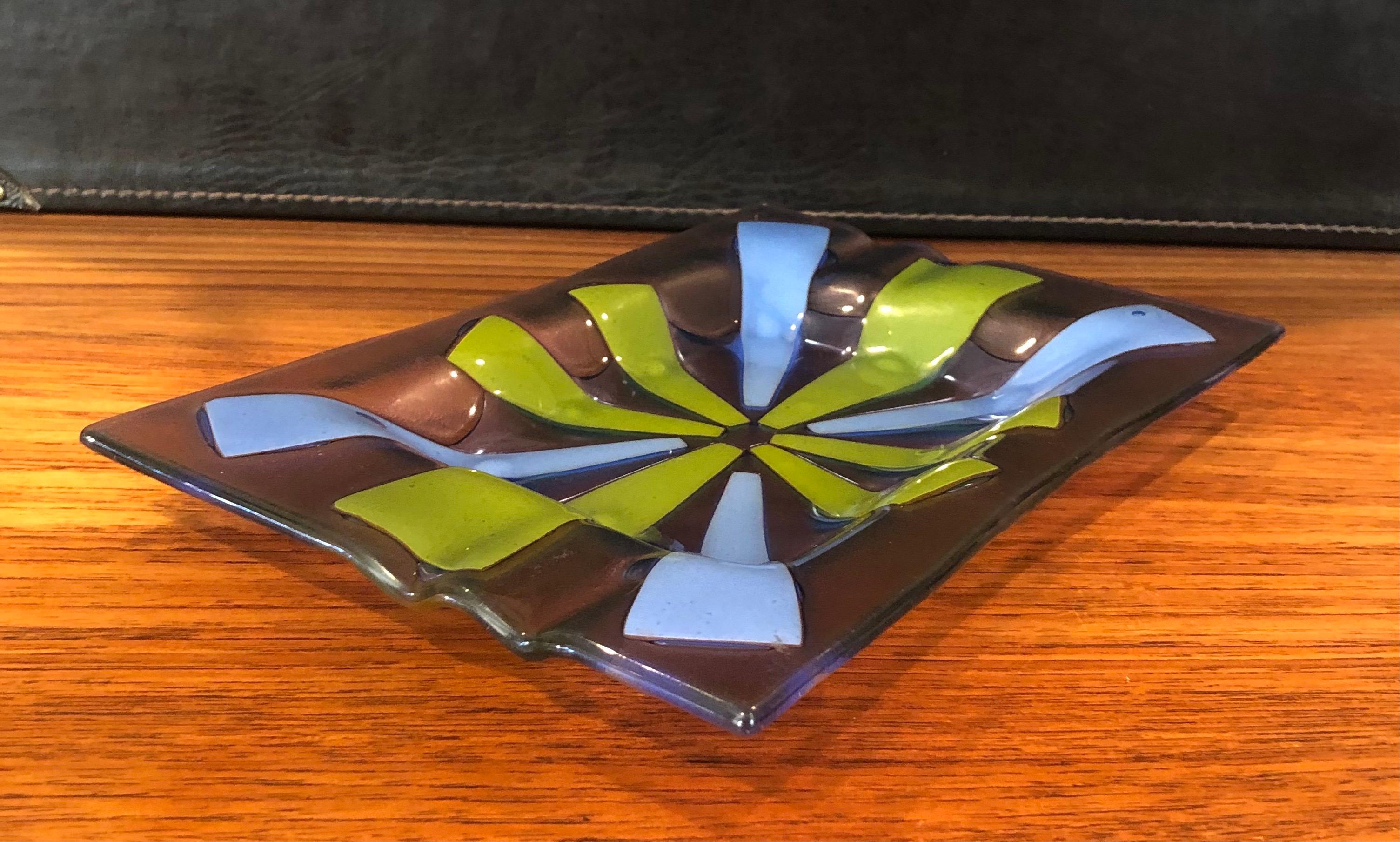 Midcentury fused art glass ashtray by Higgins, circa 1950s. The pattern, called “Tortoiseshell” is created by sandwiching enameled glass panels of periwinkle blue and avocado green between tinted lavender glass panels to create an atomic starburst