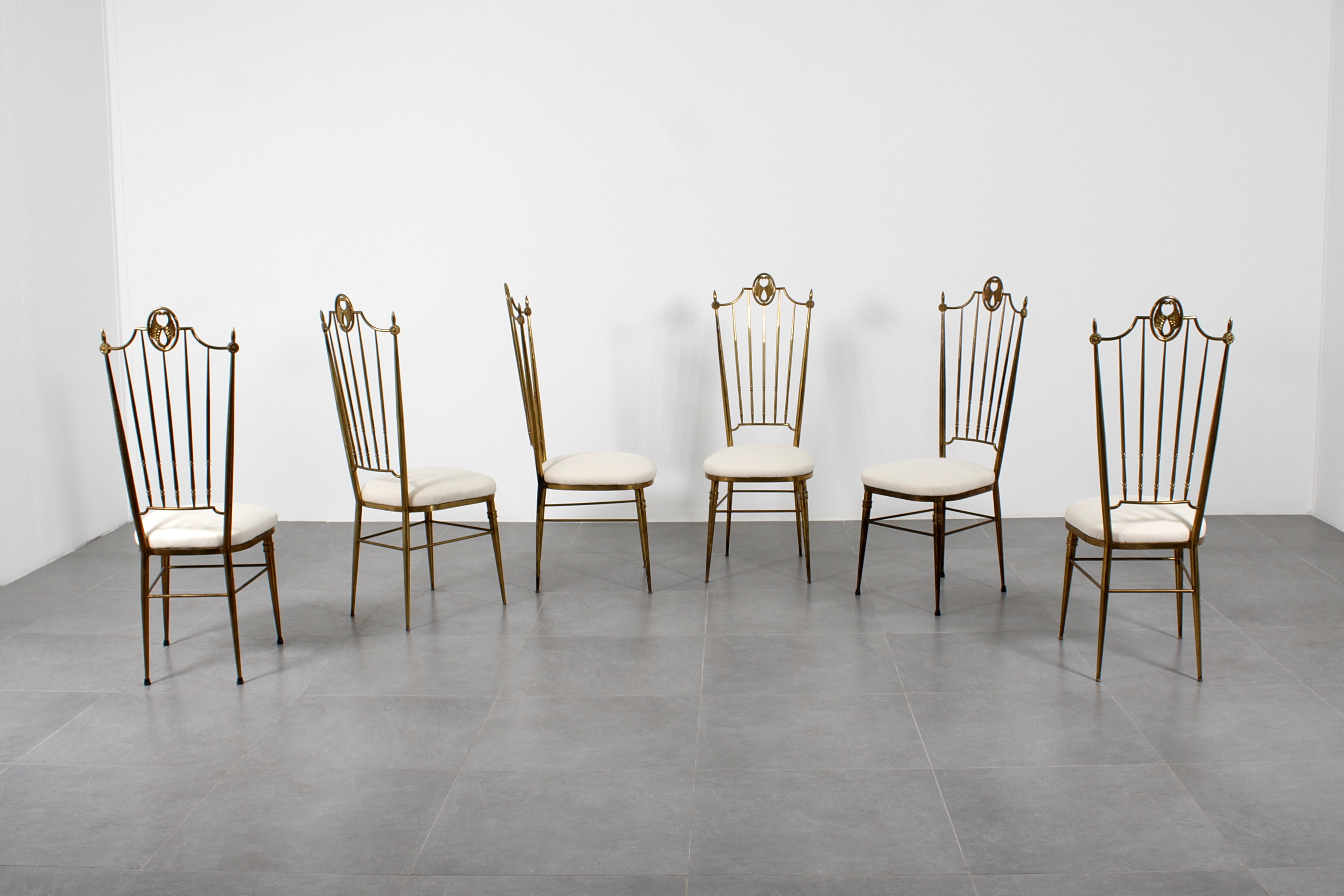 Ensemble très élégant de 6 chaises de salle à manger avec dossier haut en laiton doré et assise en tissu blanc. Lignes droites, courbes et éléments décoratifs agrémentent le design des dos entièrement en laiton.  Les chaises ont été retapissées.