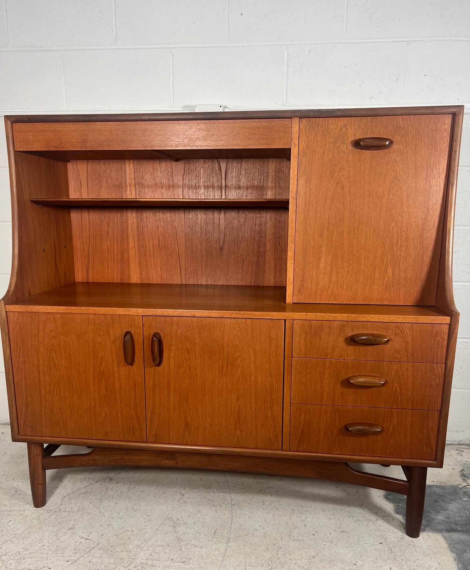 Mid century modern versatile teak highboard or server by G Plan. Featuring a drop down cabinet that can be used as a small desk and a drawer for silver ware at the top.

Three drawers and a cabinet with removable shelf at the bottom.
Very good