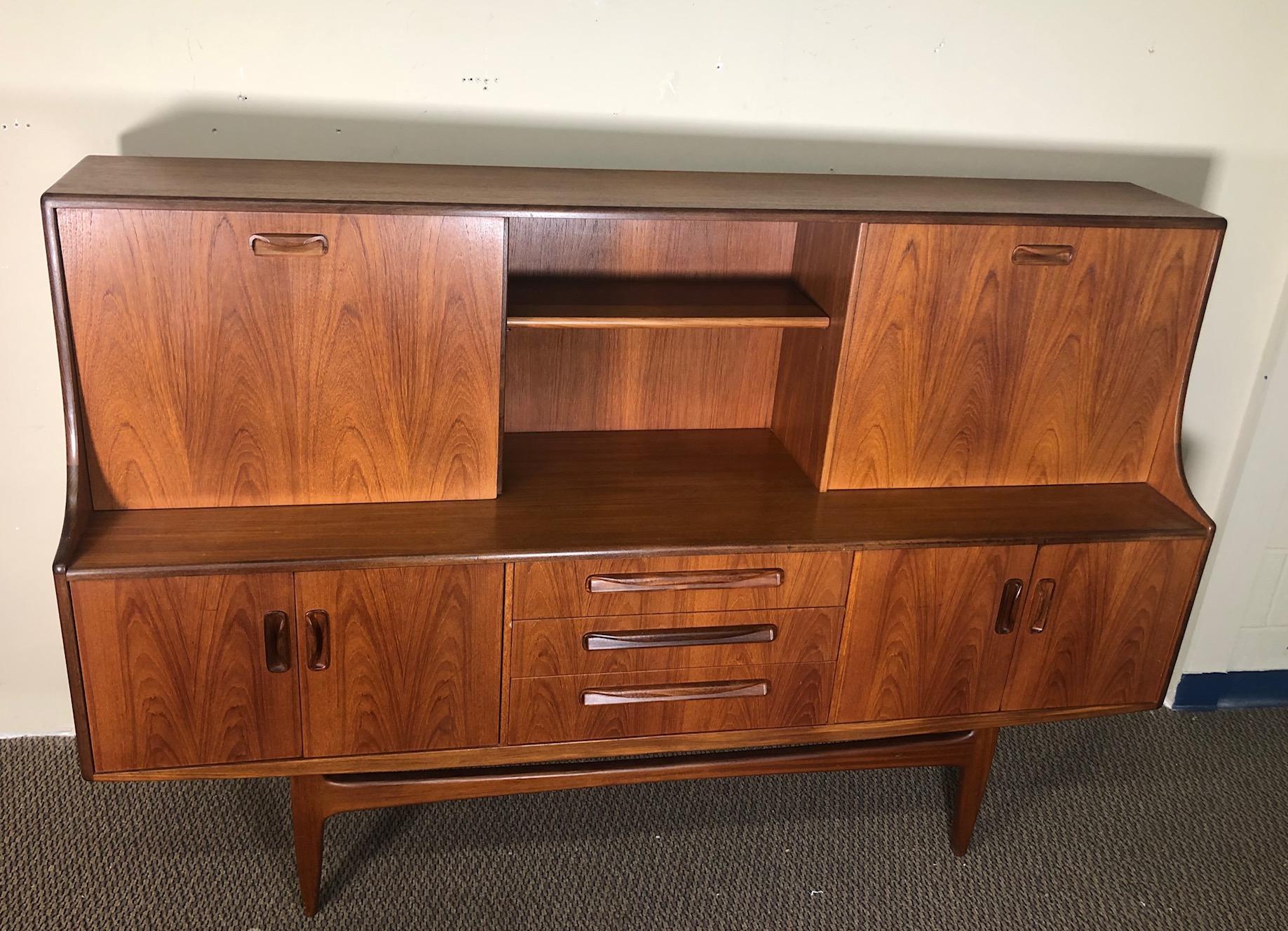 Mid-Century Modern versatile high board by G Plan. Featuring a sliding door and a small drop down desk that can comfortably hold a laptop or be used as a wine bar. Shelves are adjustable. Unfinished back.

Exceptionally nice wood grain on this