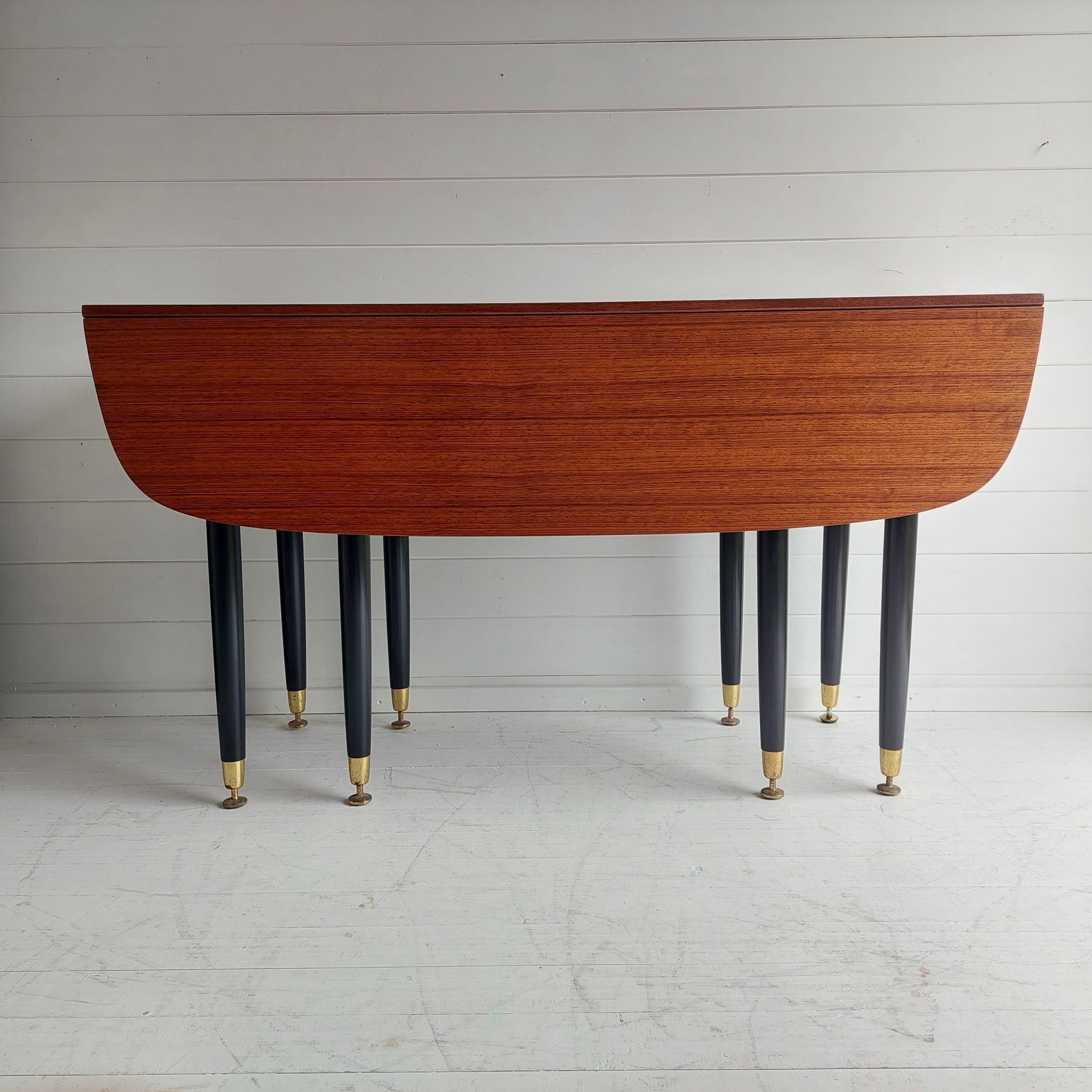 A striking example of mid century E Gomme, G plan dining furniture. 
Dated 1959 the elegant combination of black, gold and dark wood encapsulates the signature style typical of 1950's MCM design.

It is made of tola on the top and black in the