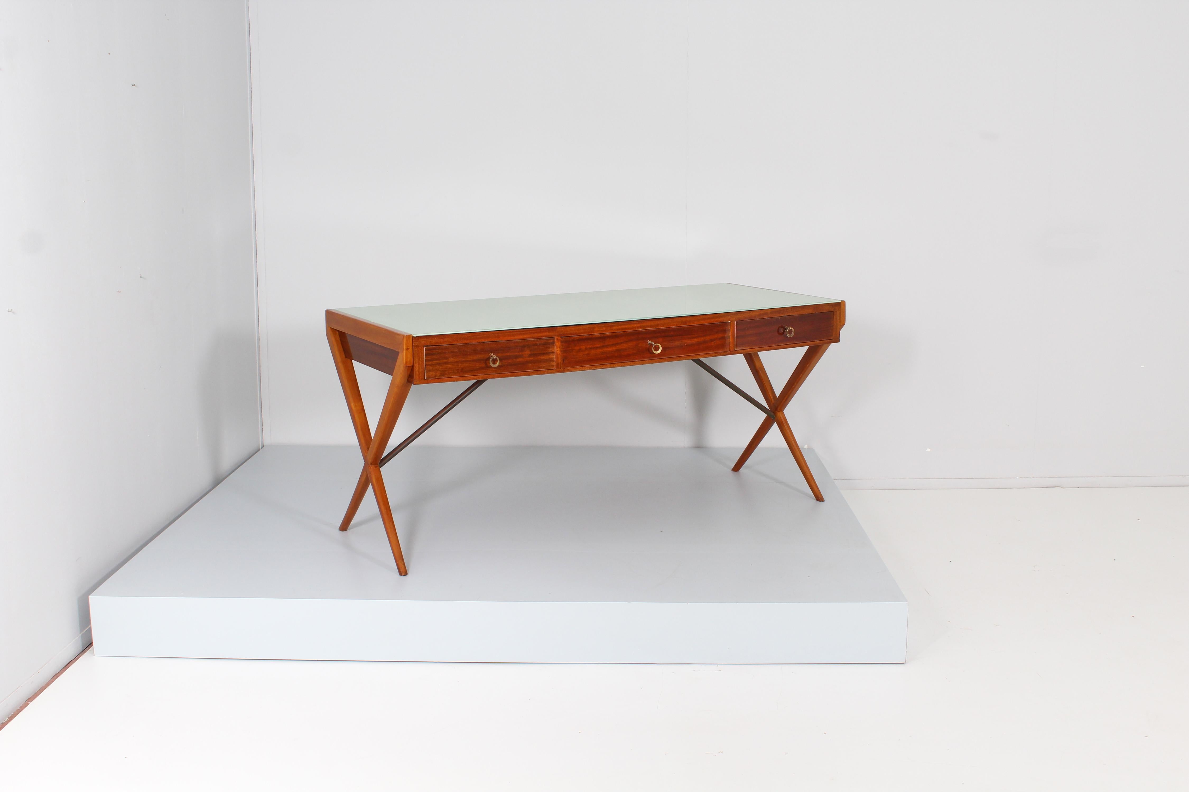 Large and elegant desk in light wood with rectangular glass top in moss green, three front drawers and crossed side legs, with brass support rods.
The captivating geometric design and the quality of the materials make it attributable to Gio' Ponti,