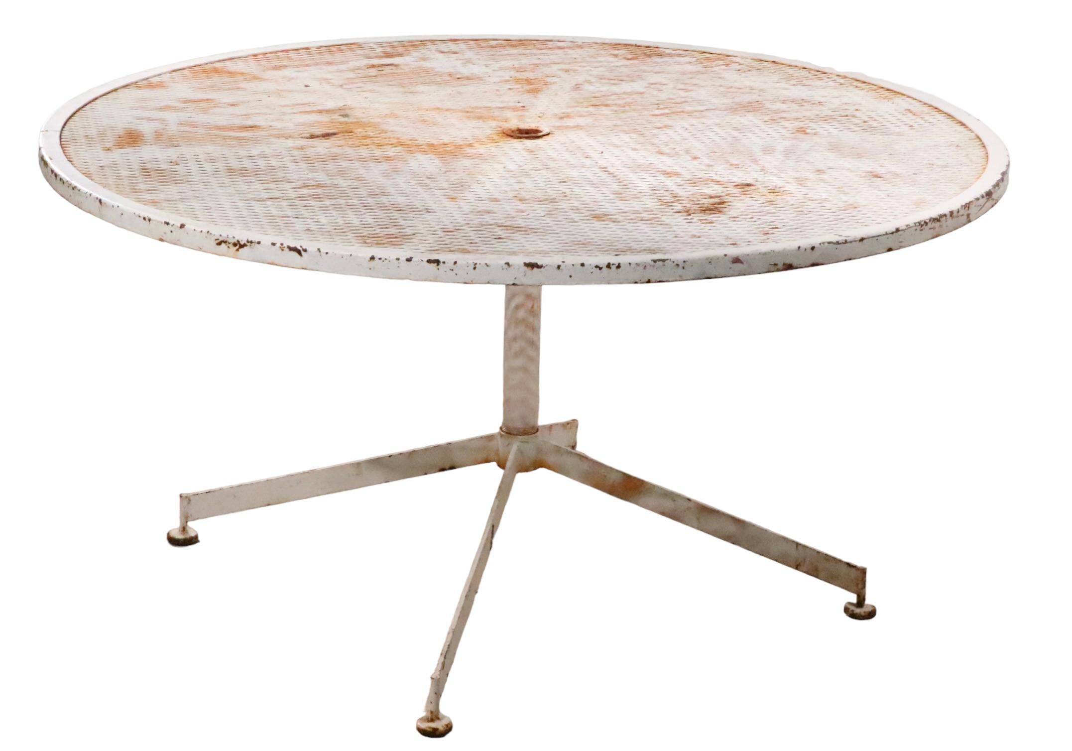 Architectural midcentury garden, patio, poolside dining table having a metal base, with metal mesh top. This chic table features a circular top, with a pedestal center post, and four radiating legs at the base. The table is structurally sound, and