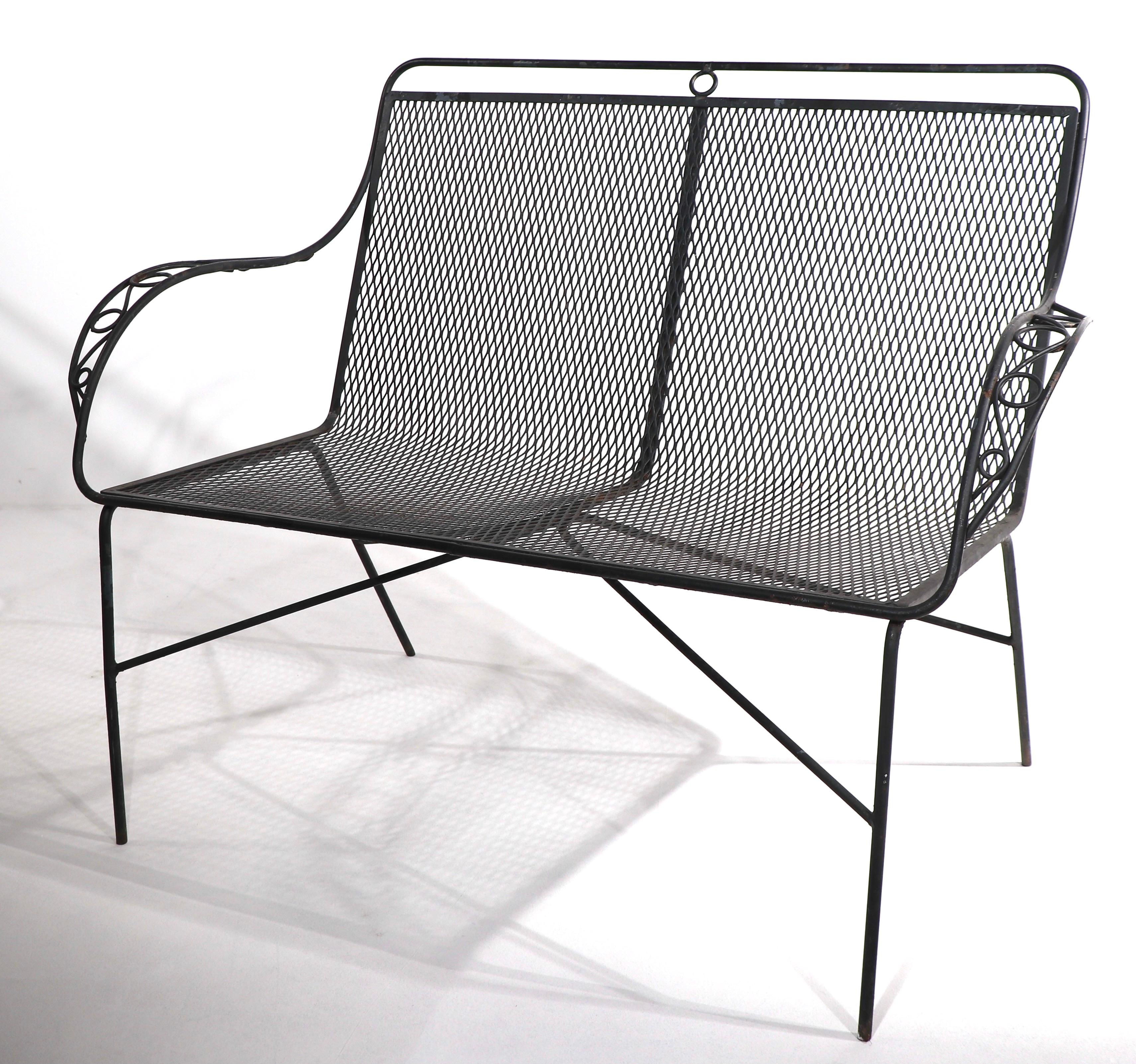 Stylish wrought iron and metal mesh loveseat settee, attributed to Woodard. This example is in very good condition, showing only light cosmetic wear, normal and consistent with age. 
Perfect for garden, patio, or poolside use, currently in later