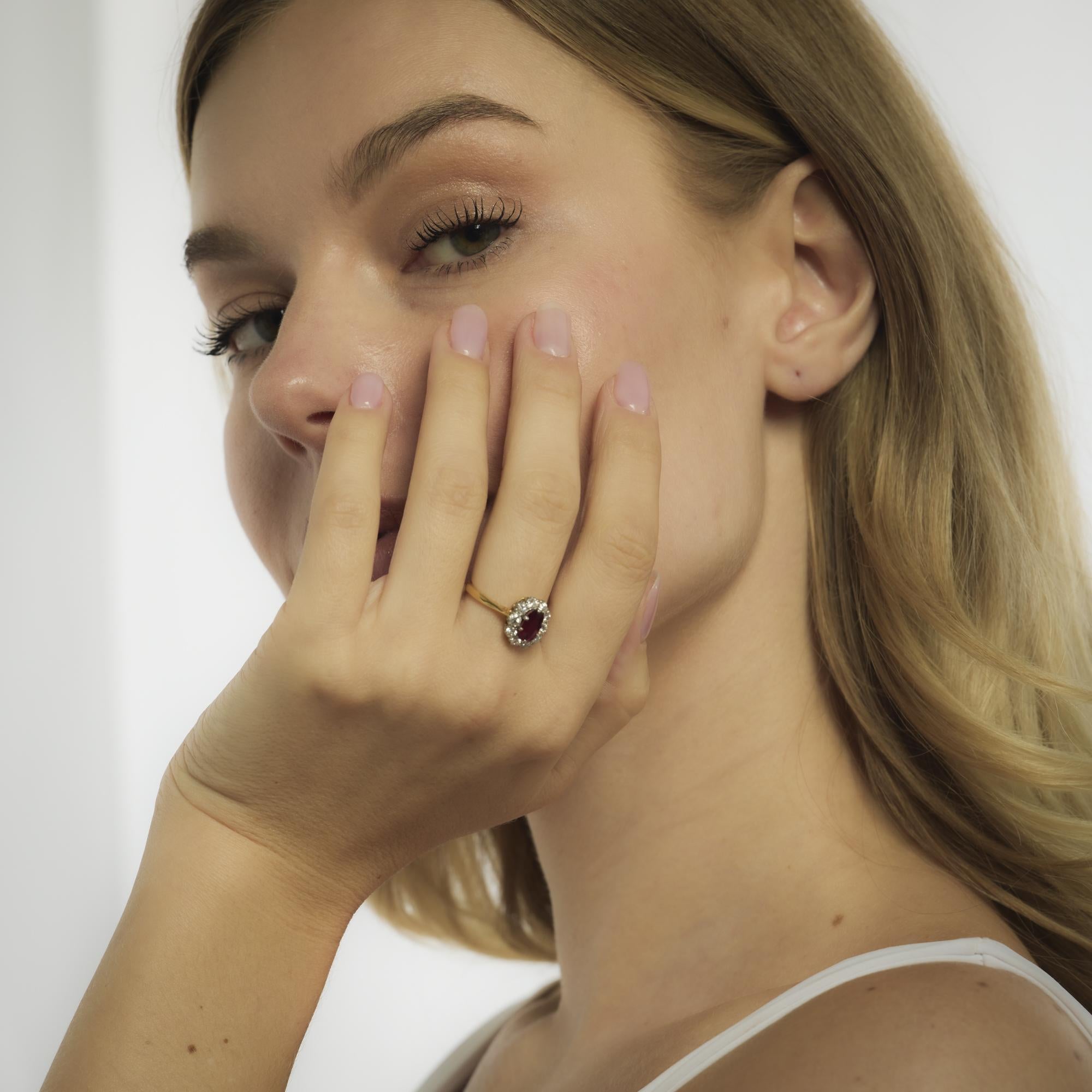 This mid-century ring from the 1950’s features a 1.00-carat oval cut ruby of Thai origin, certified by GCS #5784-3846 as unheated. Ten round brilliant cut diamonds, totaling approximately .60 carats in F-G color and VS clarity, form a radiant halo