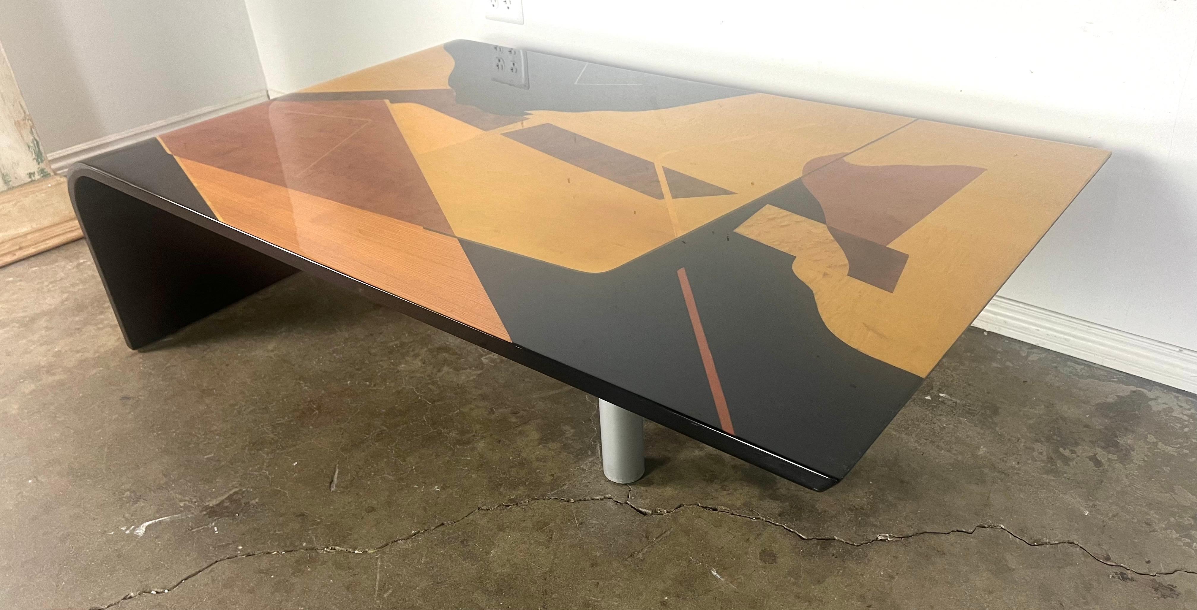 Table basse en bois laqué italien en forme de cascade avec un design abstrait.  La surface de la table présente un motif géométrique complexe avec des nuances de noir, d'auburn, de blond et de brun, créant une esthétique audacieuse et contemporaine,