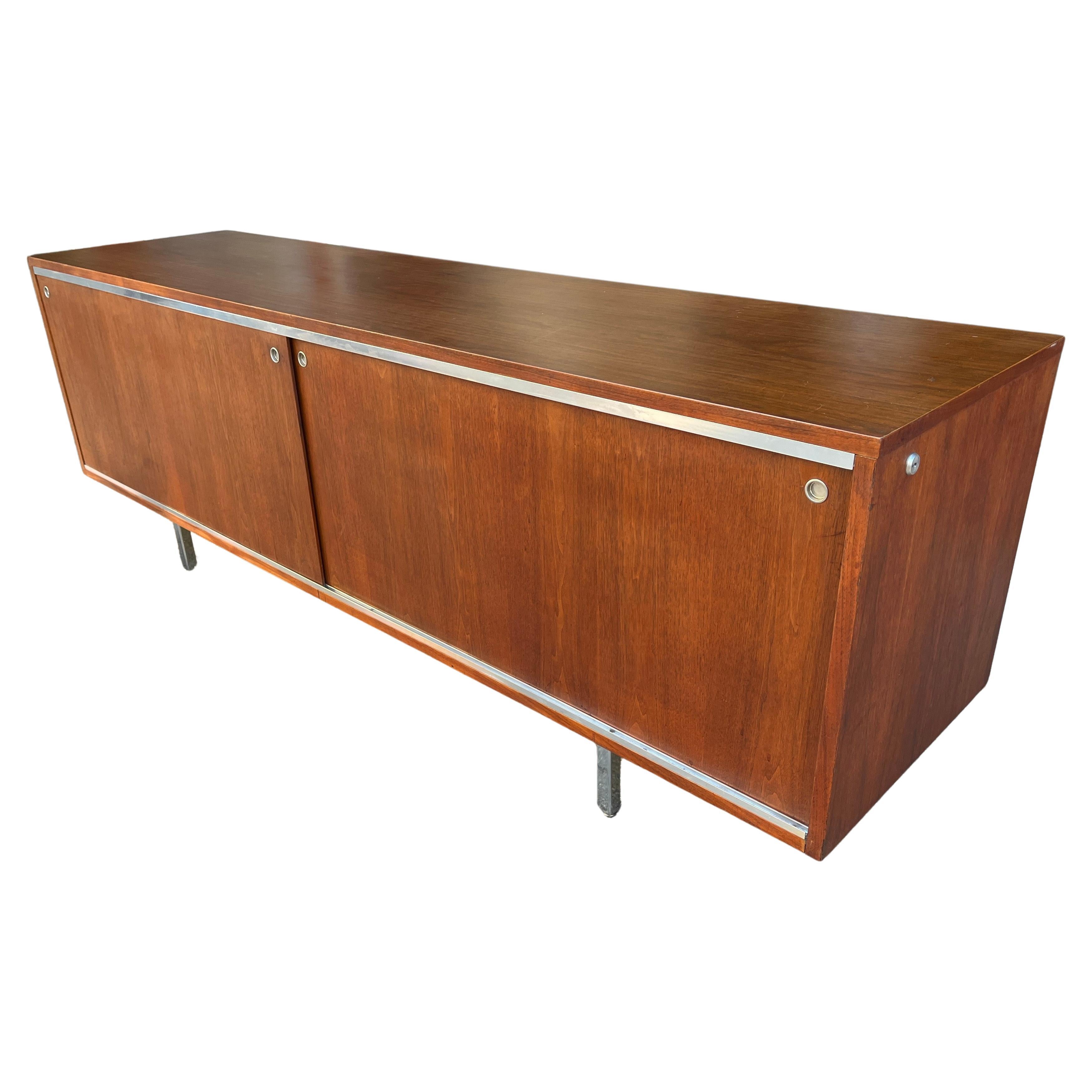 Wonderful low cabinet by Herman Miller designed by George Nelson. This beautiful brown walnut long low credenza features 2x front original walnut sliding doors with 4 sections inside and (1) adjustable shelf in each side, one file cabinet, and one